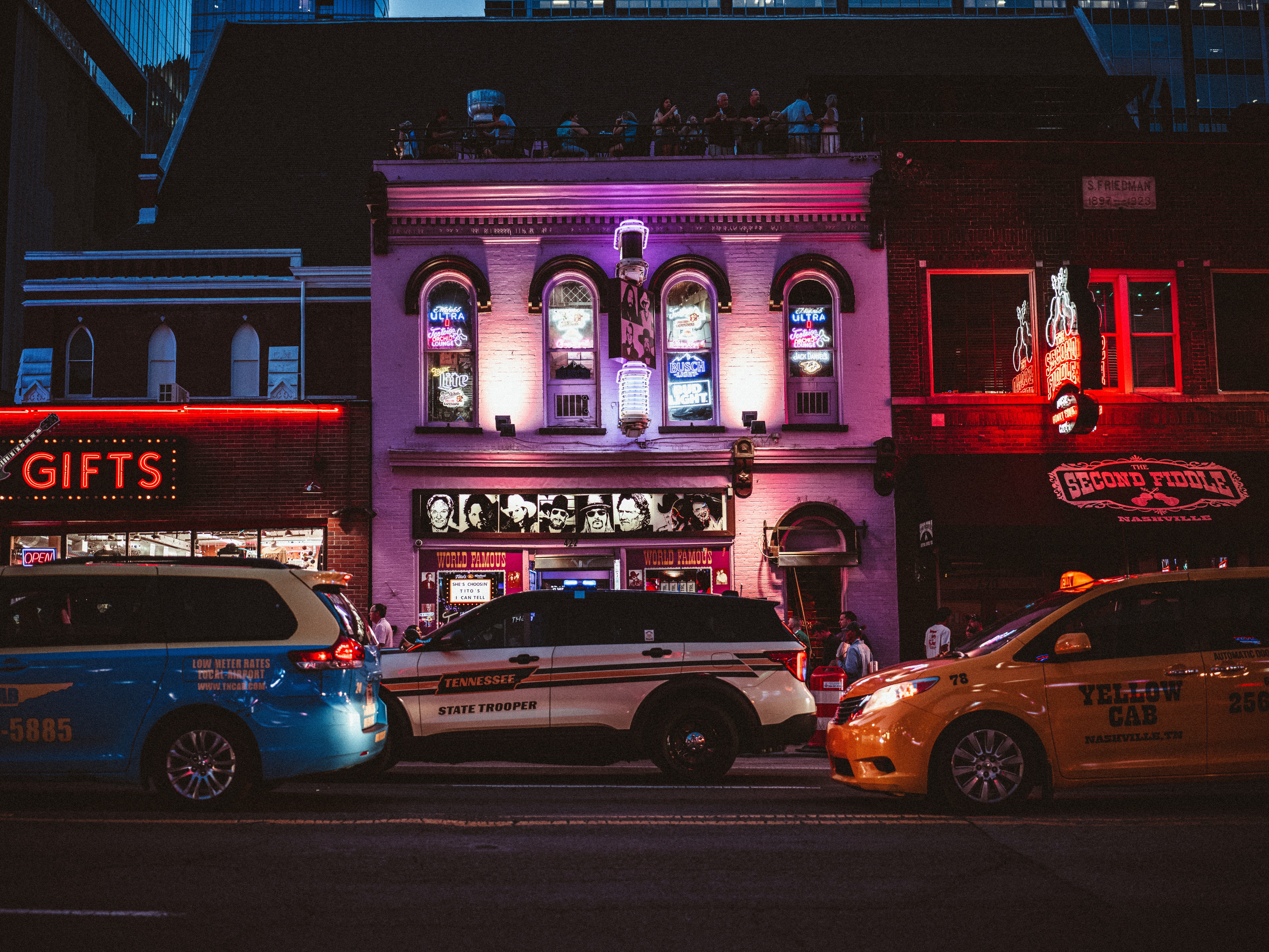 A neon-lit historic building facade in Nashville with police cars parked in front at night, red and purple stage lights illuminating the brick storefront.
