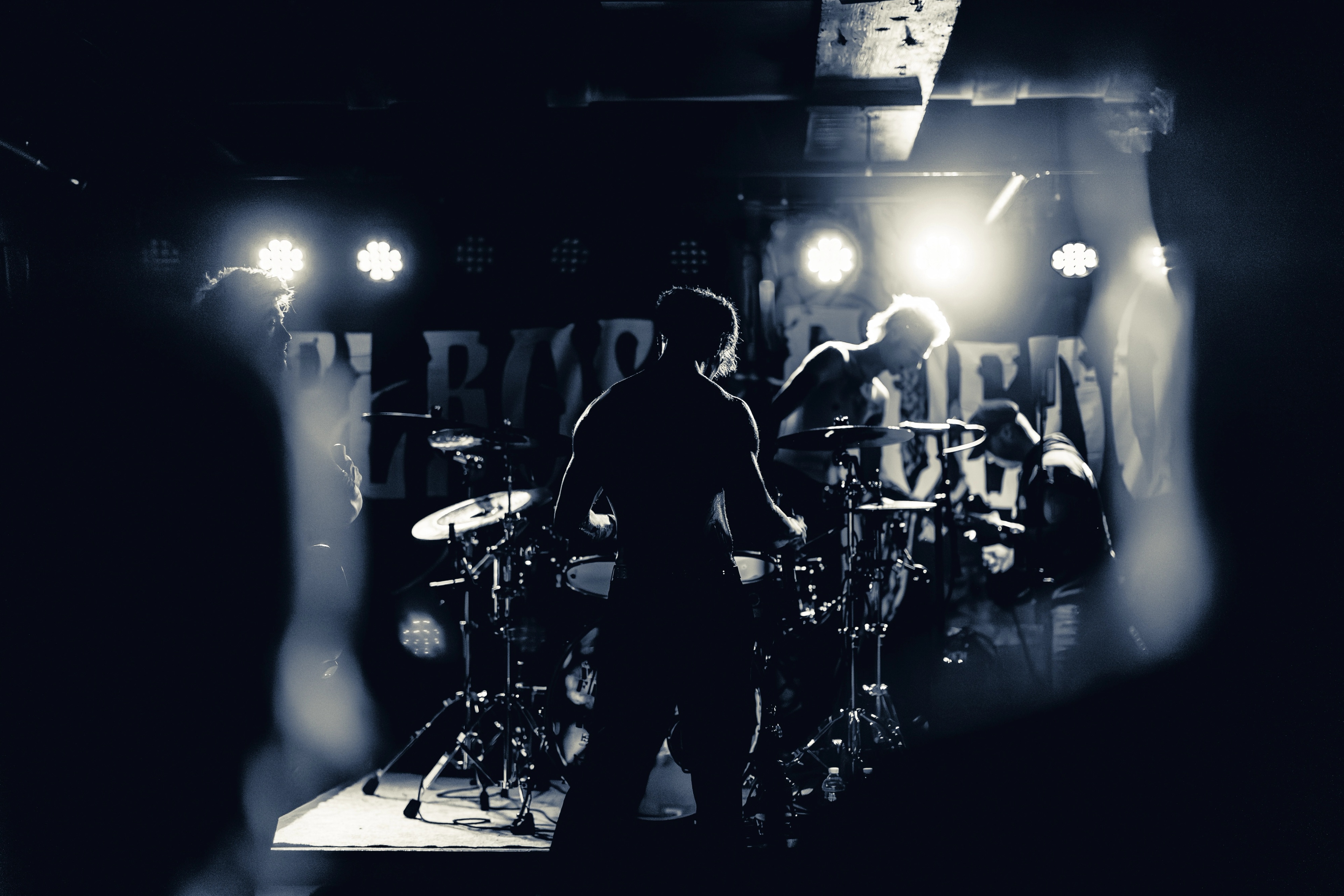A band performs on stage shrouded in smoke, backlit by bright stage lights, silhouetted against a dark venue backdrop.