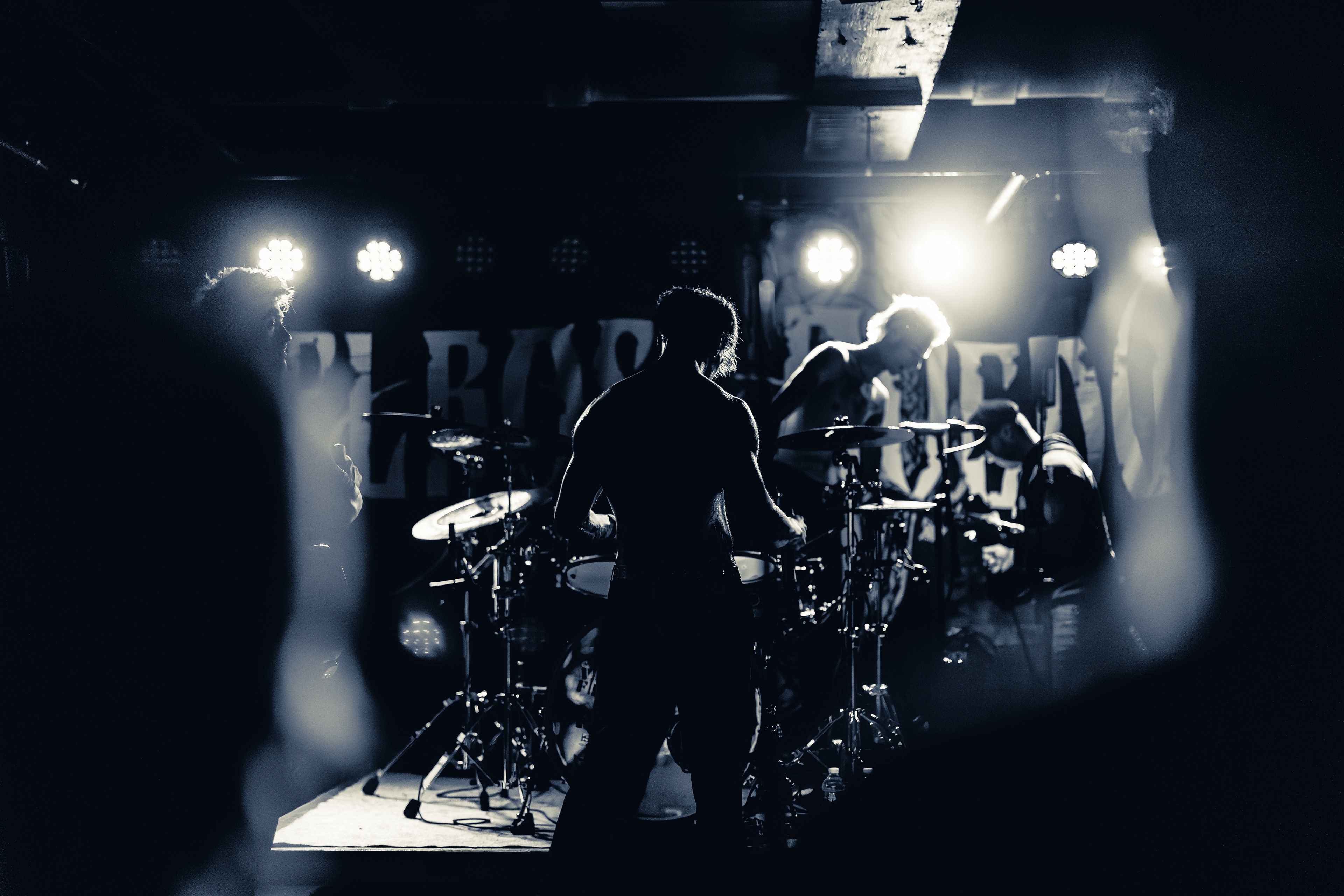 A band performs on stage shrouded in smoke, backlit by bright stage lights, silhouetted against a dark venue backdrop.