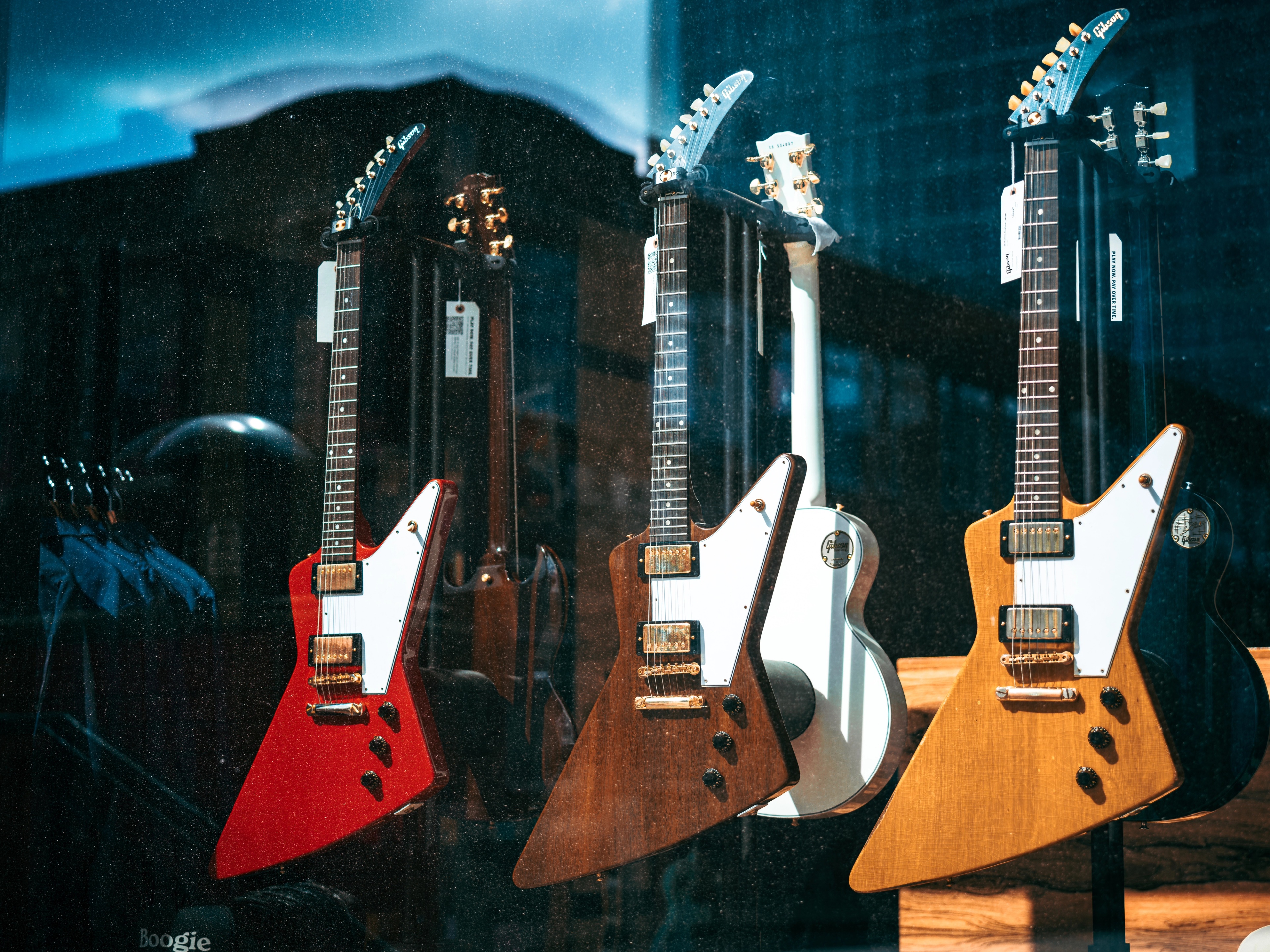 Four electric guitars with distinctive body shapes displayed in a row, featuring red, brown, white, and natural wood finishes with chrome hardware.