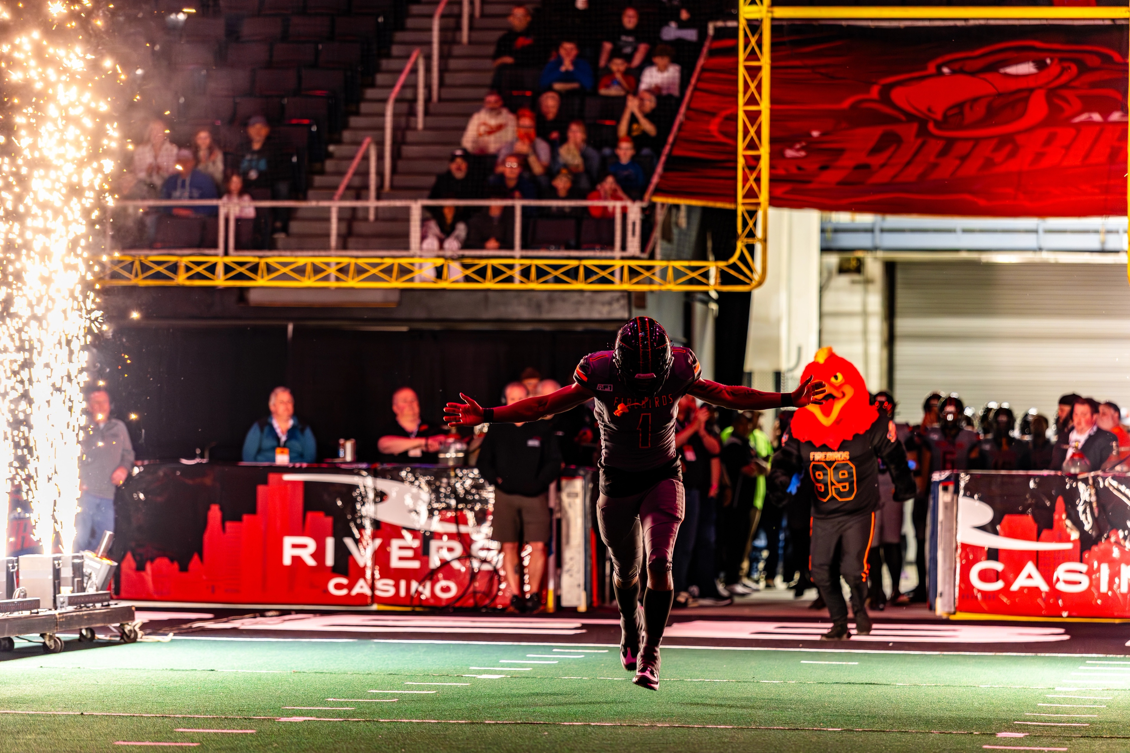 An athlete runs onto an indoor field with arms spread wide, surrounded by pyrotechnics and crowds at MVP Arena during a live sports event.