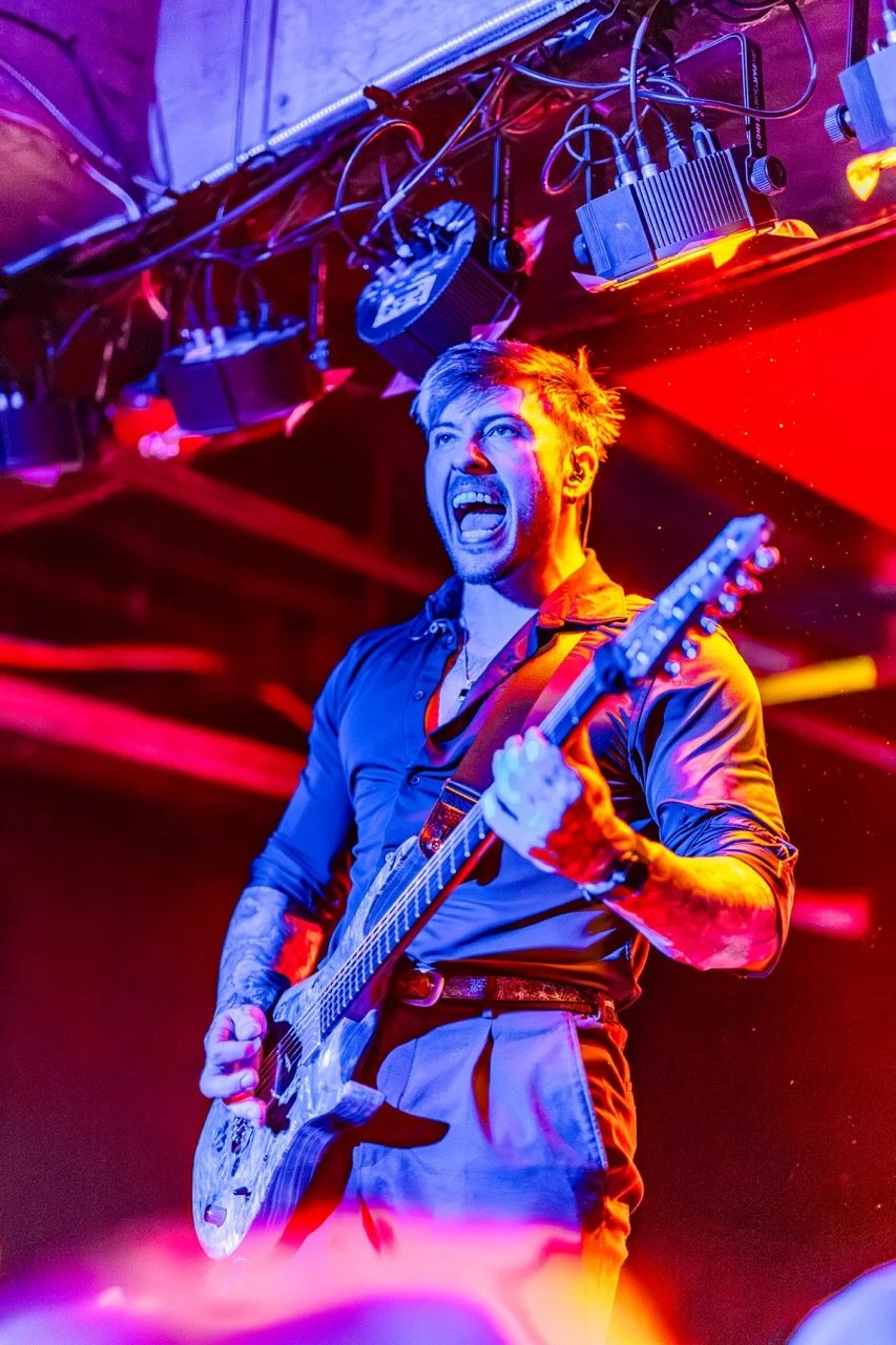 A guitarist performs on stage at Empire Live, bathed in red and blue neon lighting, mouth open mid-shout while playing an electric guitar.