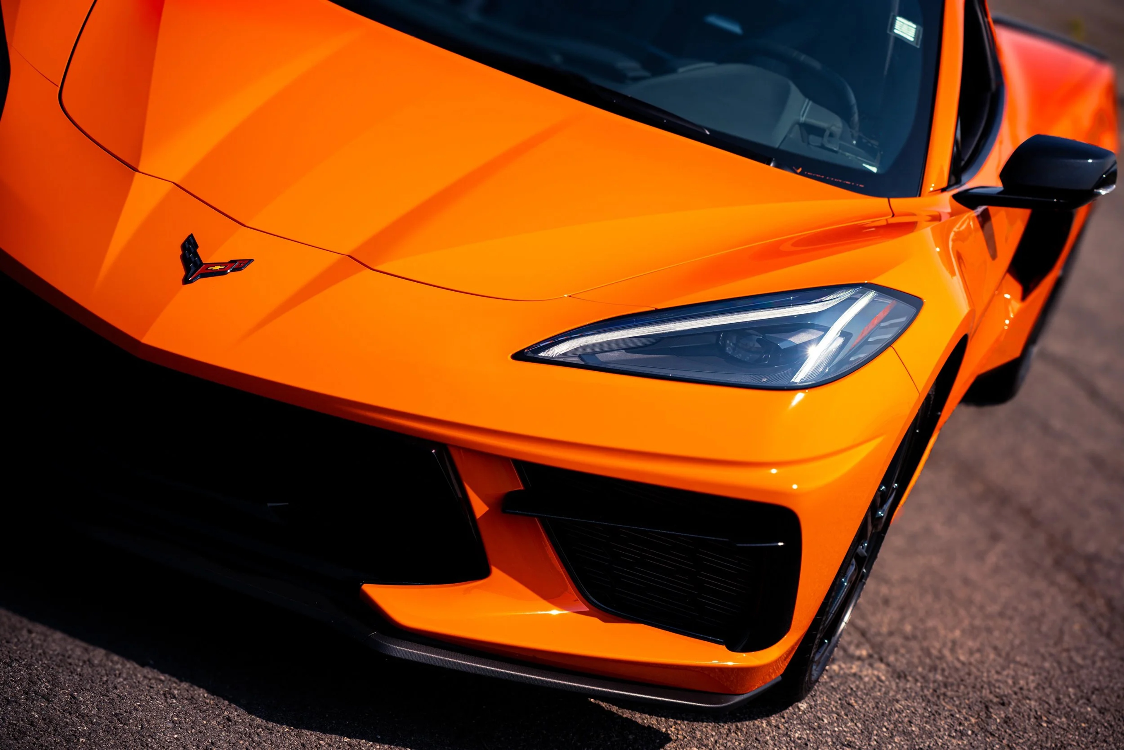 A bright orange Chevrolet Corvette photographed from the front three-quarter angle, showing aggressive headlights and aerodynamic bodywork in daylight.