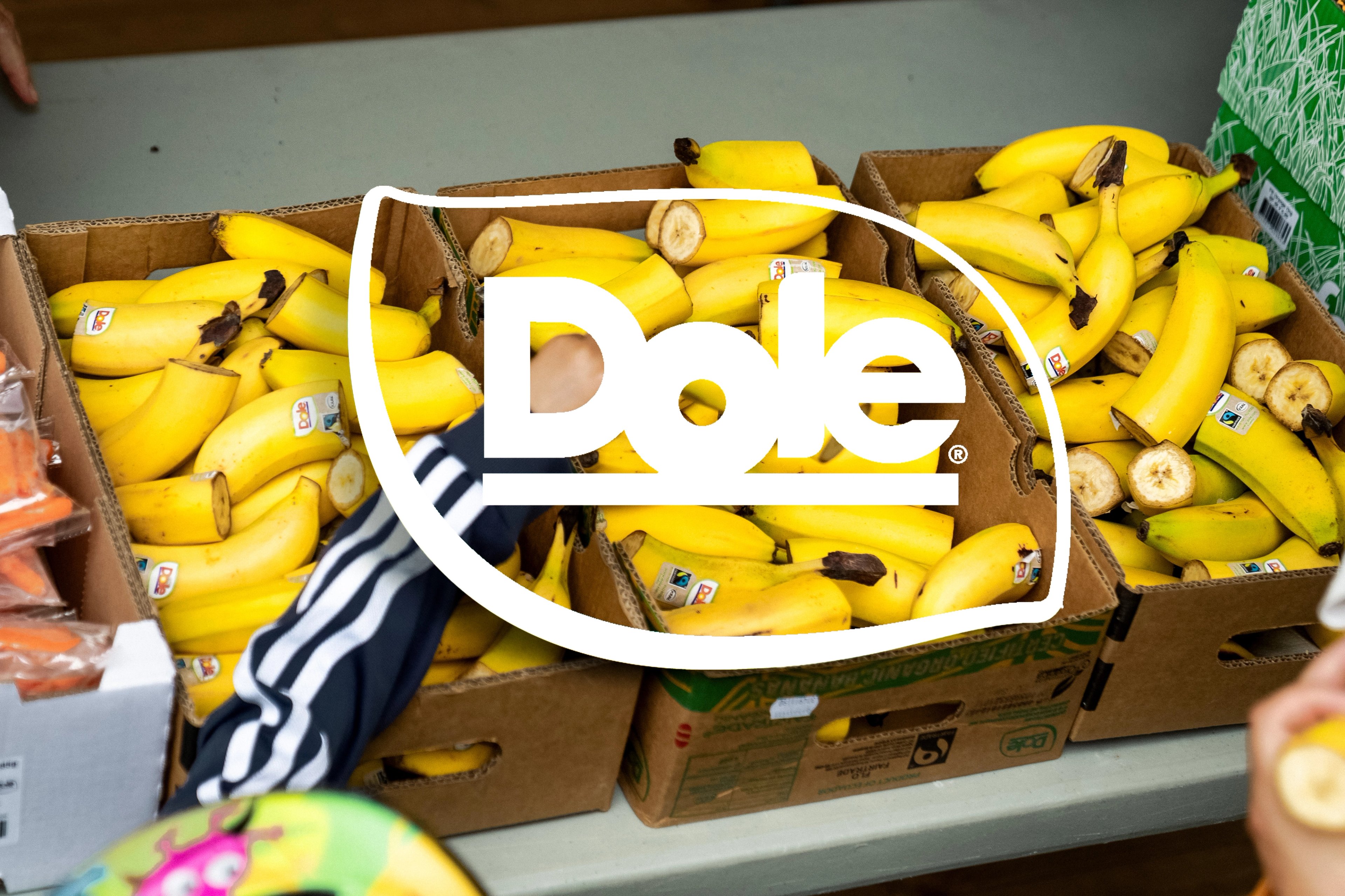 Boxes of yellow bananas, some being picked up, with the white Dole logo overlaid.