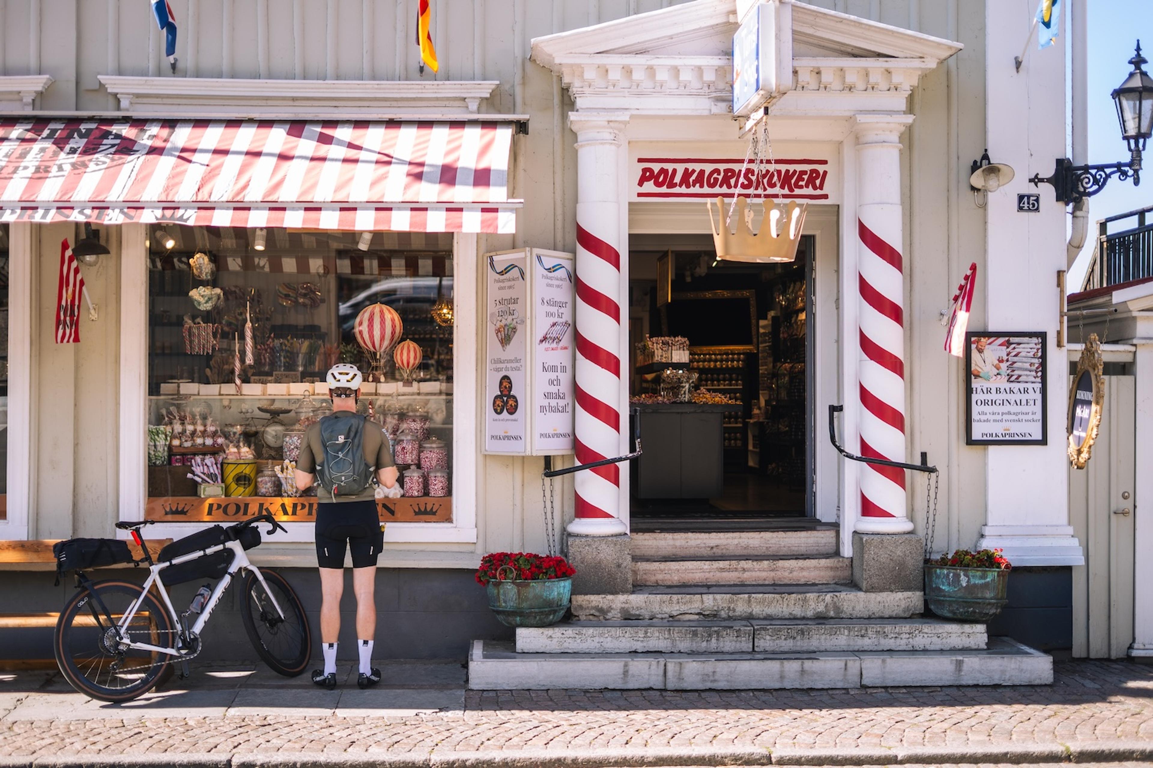 A cyclist and their bike are in front of a candy store with red and white striped columns and awning.
