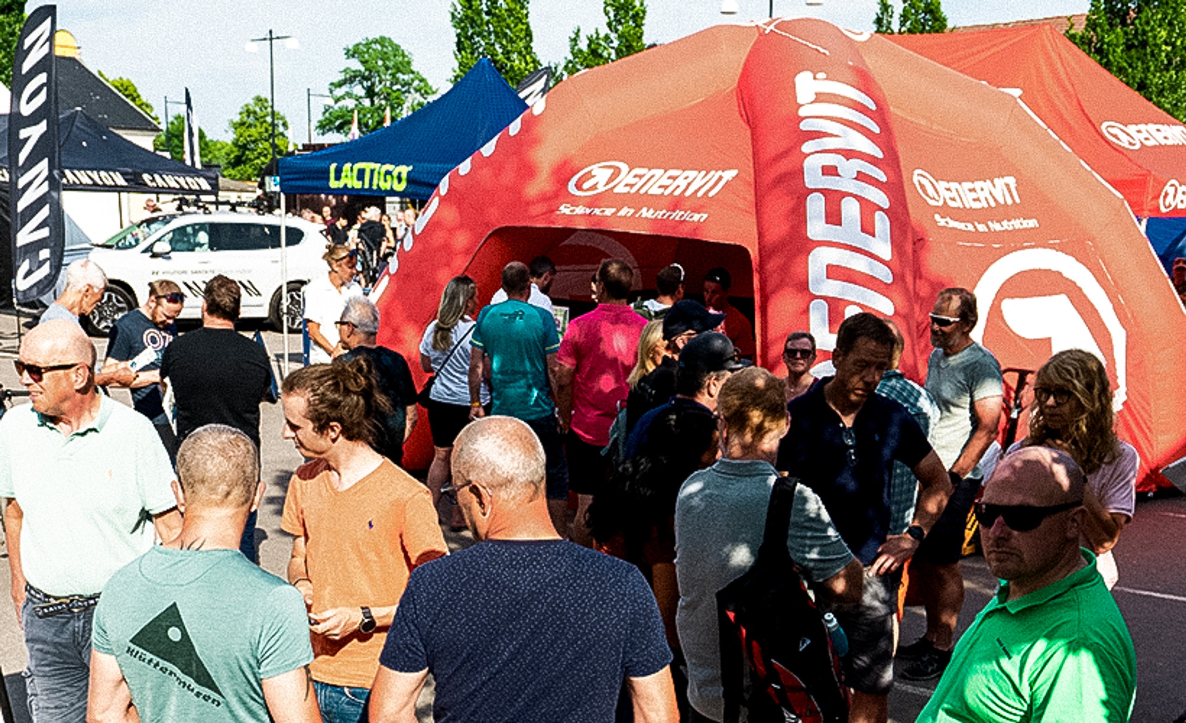 A crowd of people gathered around red and blue branded tents at an outdoor event.