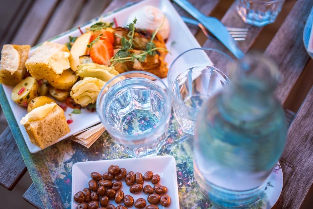 A rustic wooden table set with a plate of bread, potatoes, and salad, along with water glasses, a bottle, and chocolate candies.