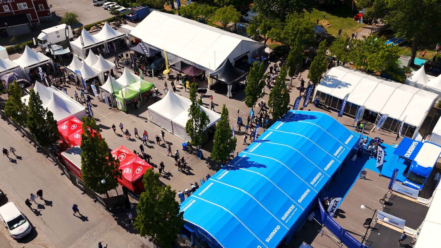 Aerial view of an outdoor event with numerous tents, people, and a large blue Shimano-branded tent.