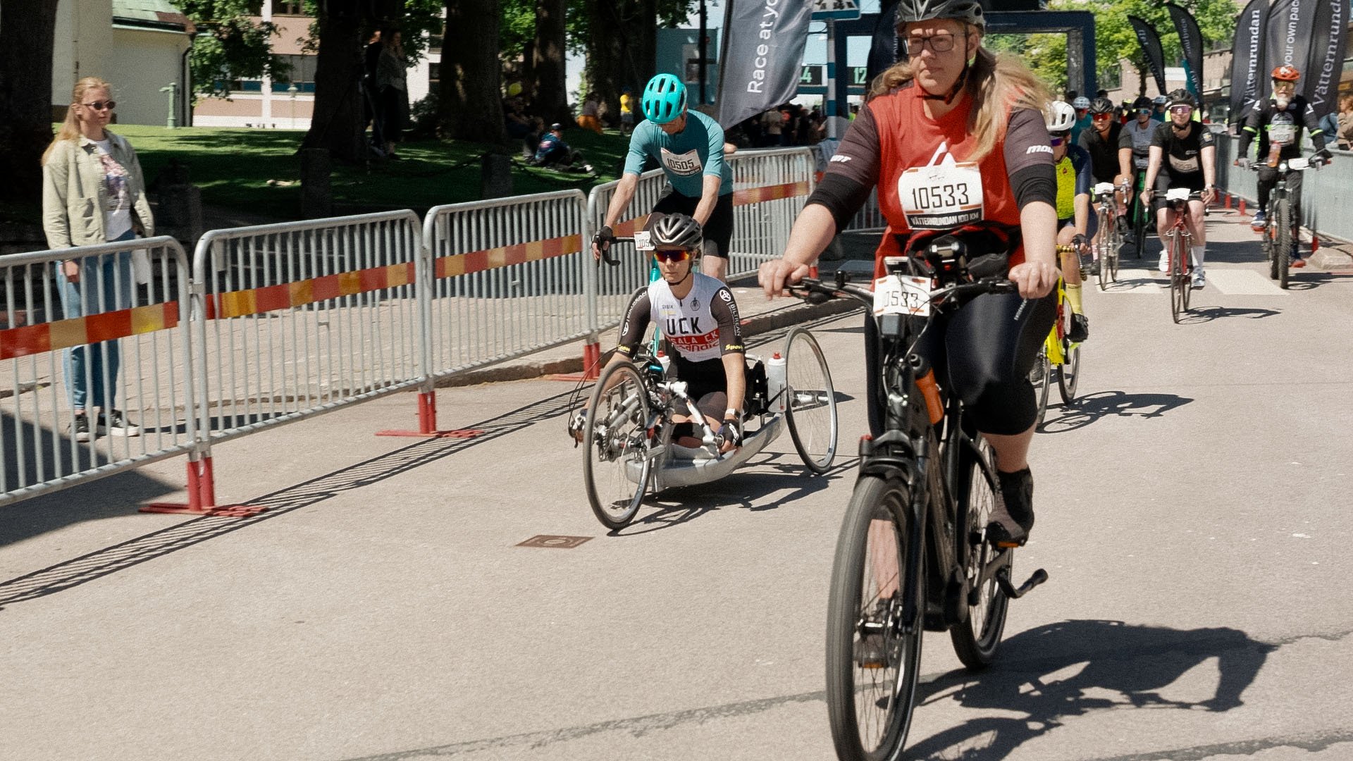 Participants in a cycling race, including a woman on an electric bike and a handcyclist.