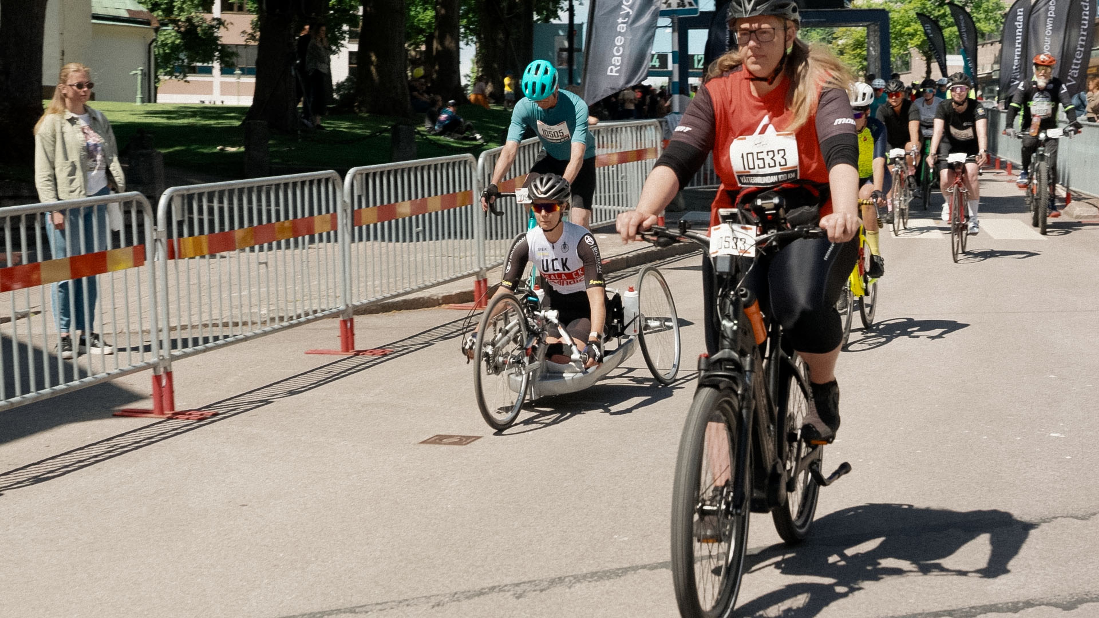 Participants in a cycling race, including a woman on an electric bike and a handcyclist.