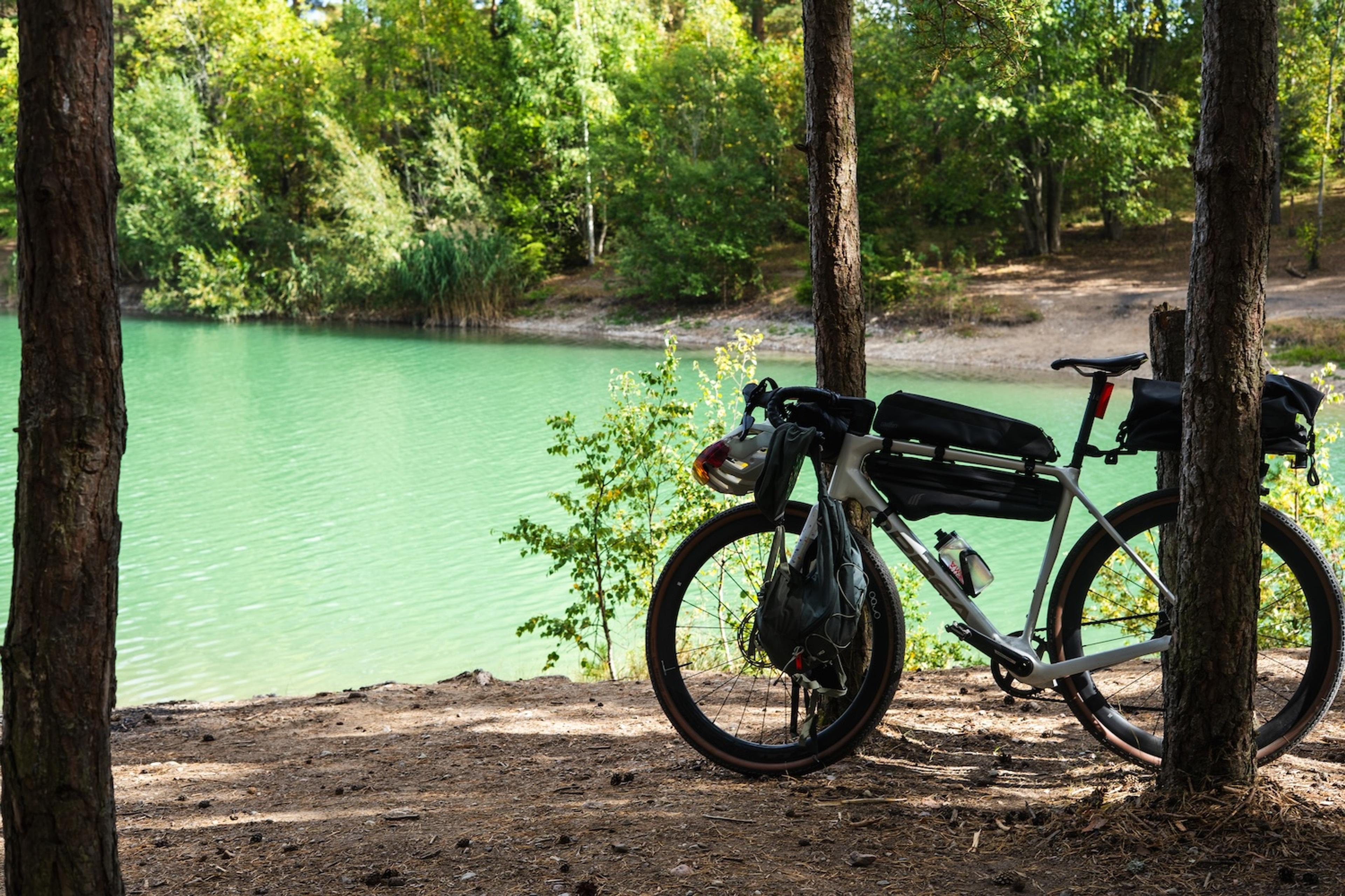 A bikepacking bike stands next to a turquoise lake in a forest.