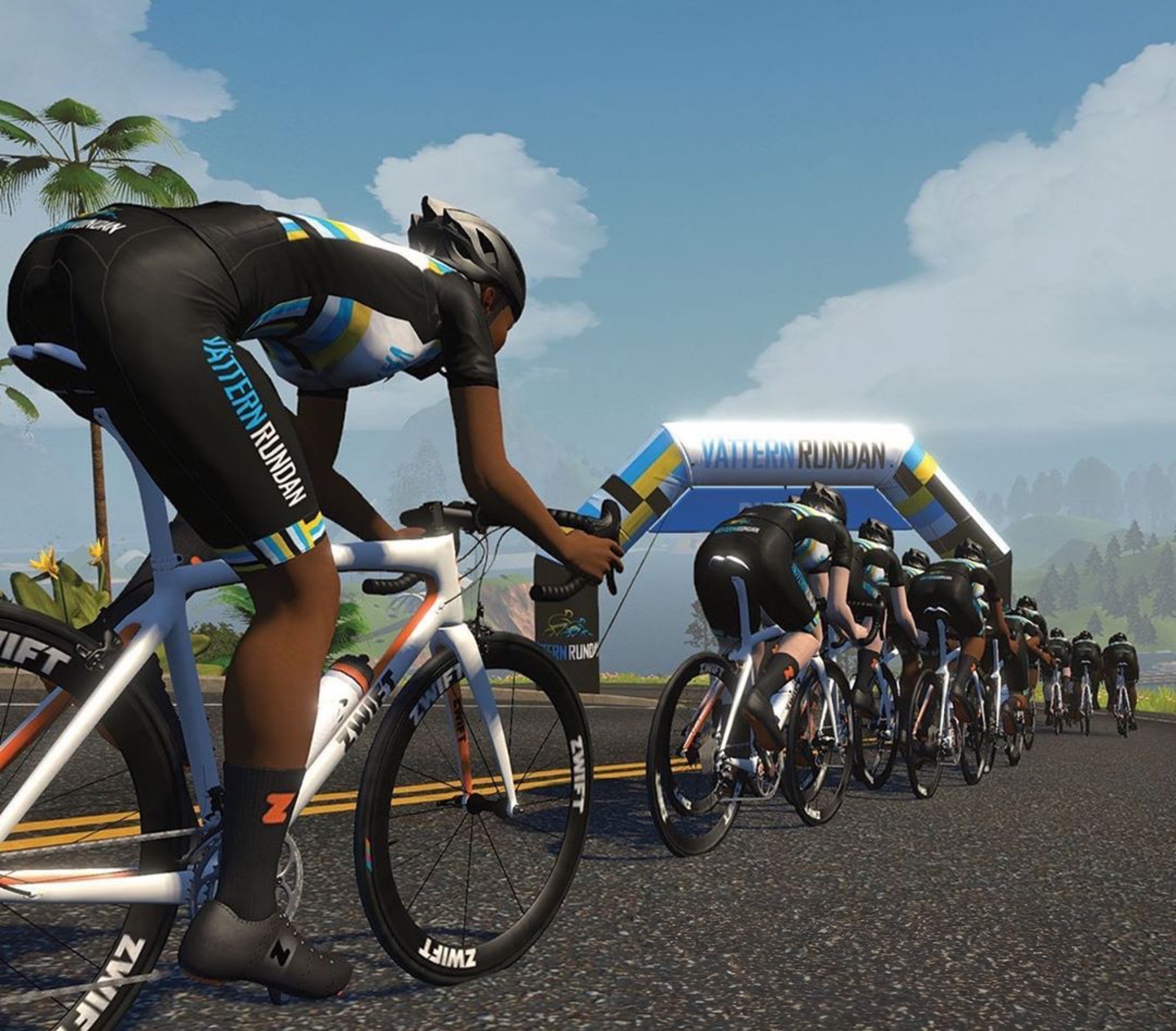 A virtual cyclist in a black, blue, and yellow "Pattern Rundan" kit leads a pack of riders on a road towards a "Vätternrundan" archway under a blue sky.
