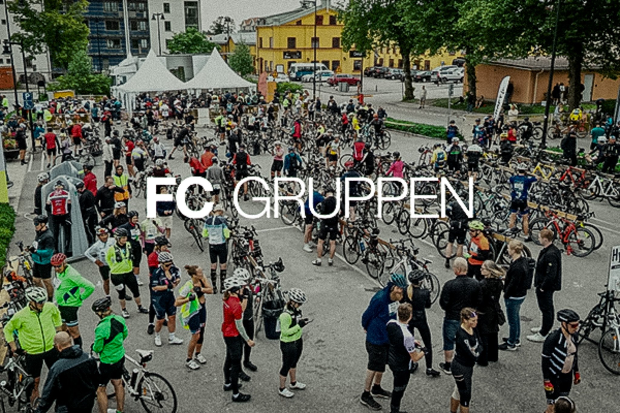 A large crowd of cyclists and their bicycles at an outdoor event, with the text "FC GRUPPEN" overlaid.