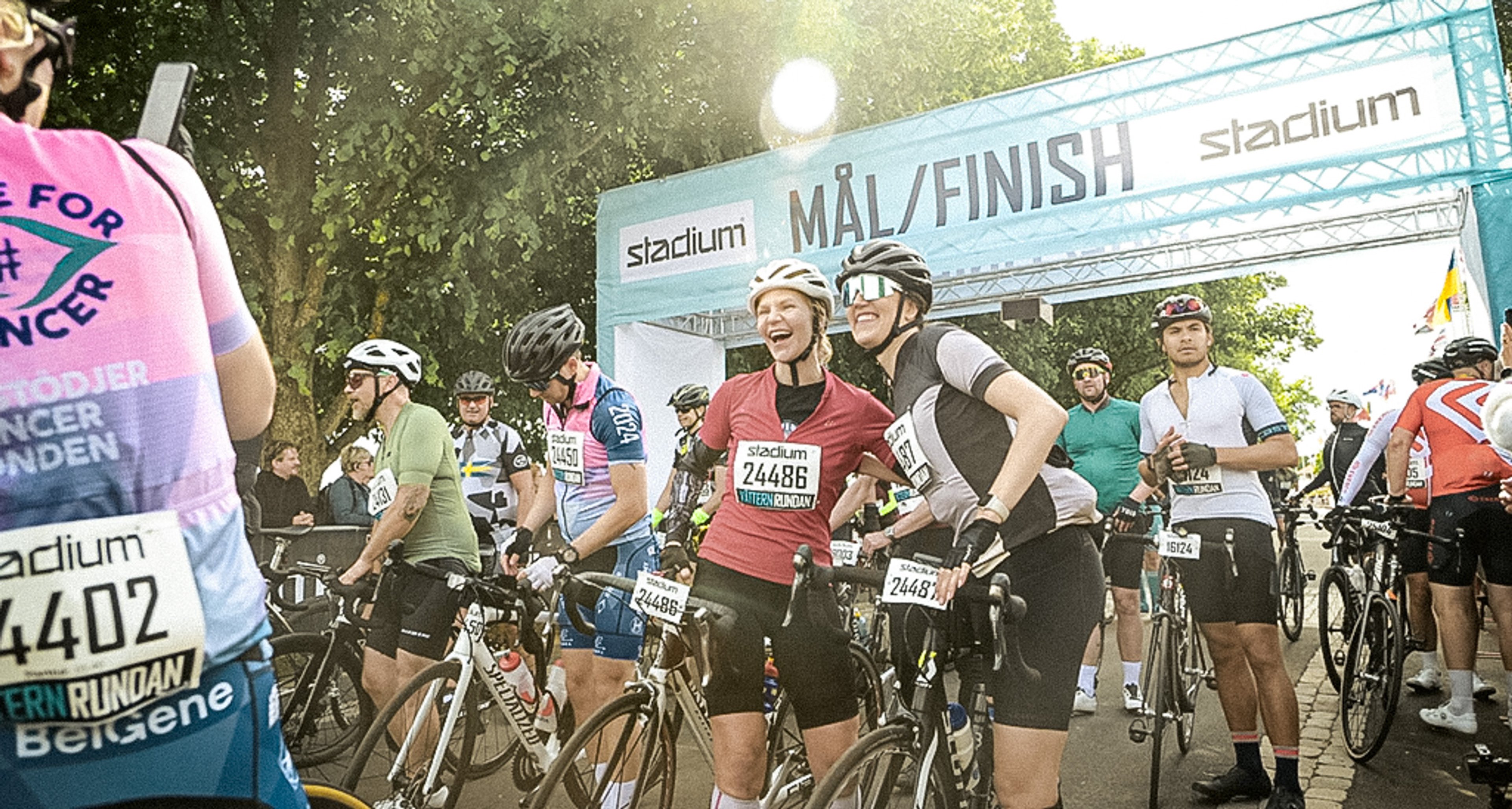 Cyclists, some smiling, pose with their bikes under a "MÅL/FINISH" banner sponsored by Stadium.