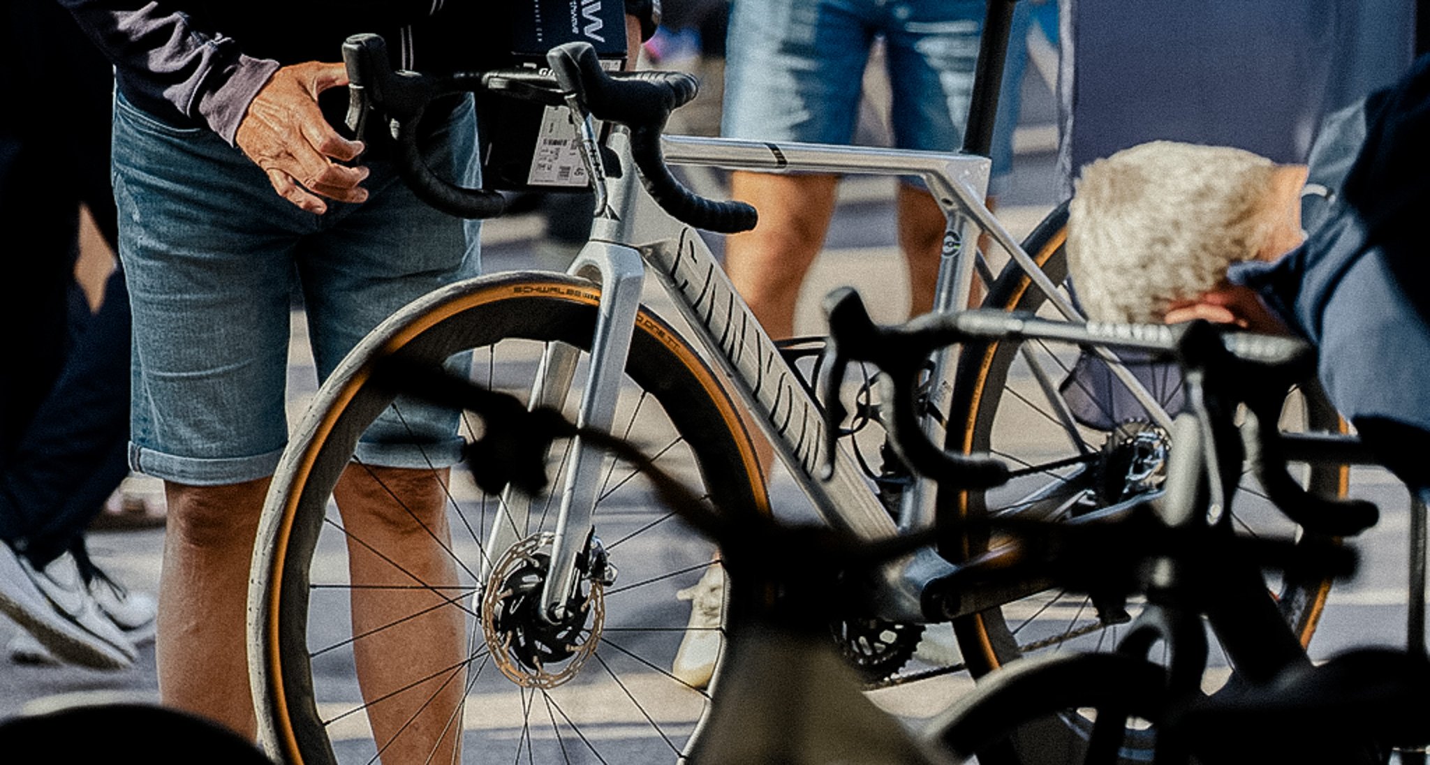 A person in jean shorts stands next to a silver road bike.