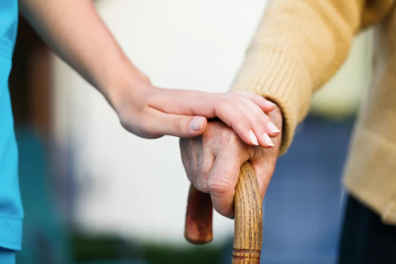 A close-up of a young person's hand gently resting on an elderly person's hand holding a cane, symbolizing the support and security provided by retirement insurance throughout life