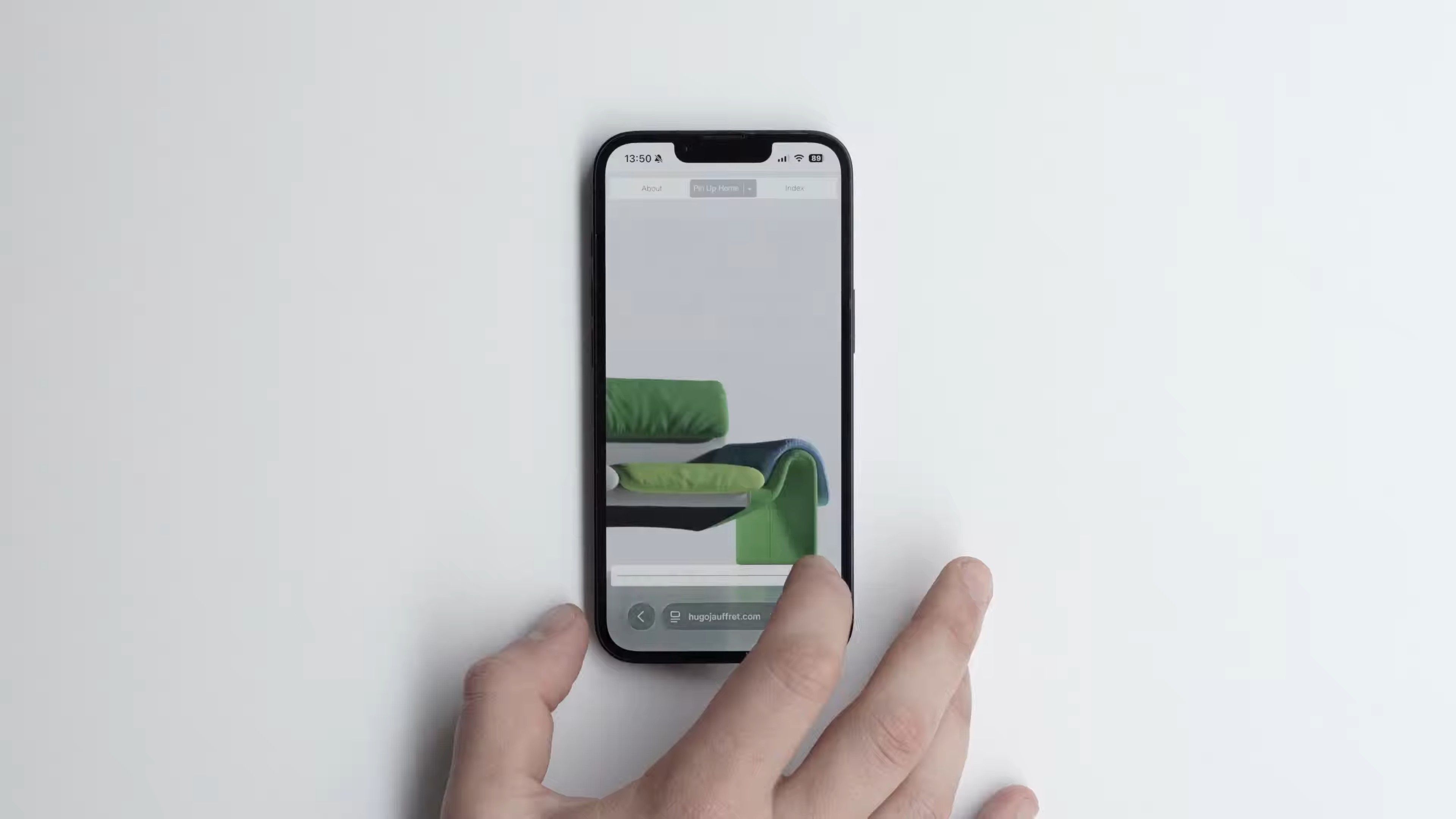 Hand holding an iPhone on a pale surface, showing photographer Hugo Jauffret’s portfolio on a still life of a stacked, green and navy seat.