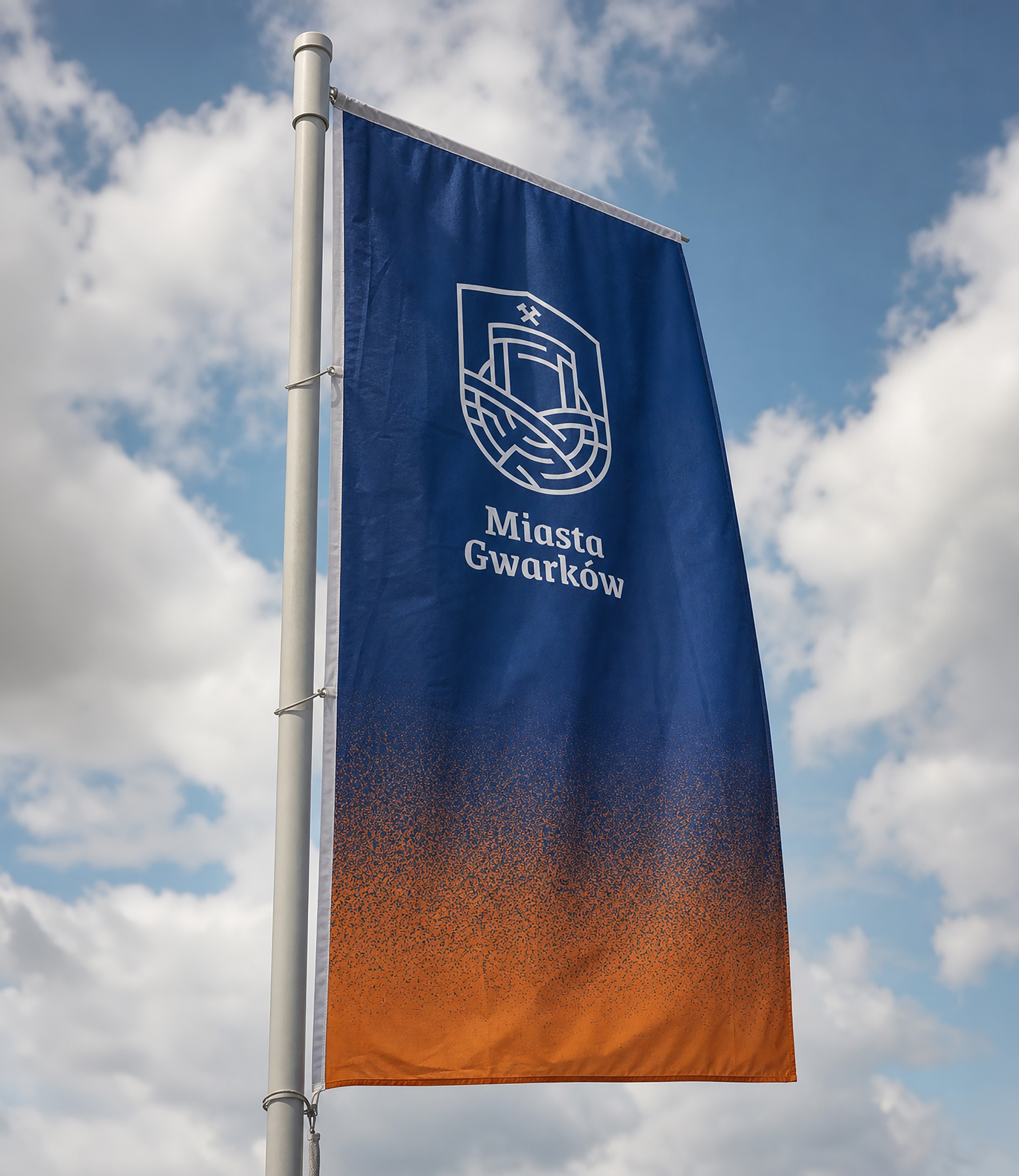 A navy-and-orange Miasta Gwarków flag with the emblem on a mast against the sky