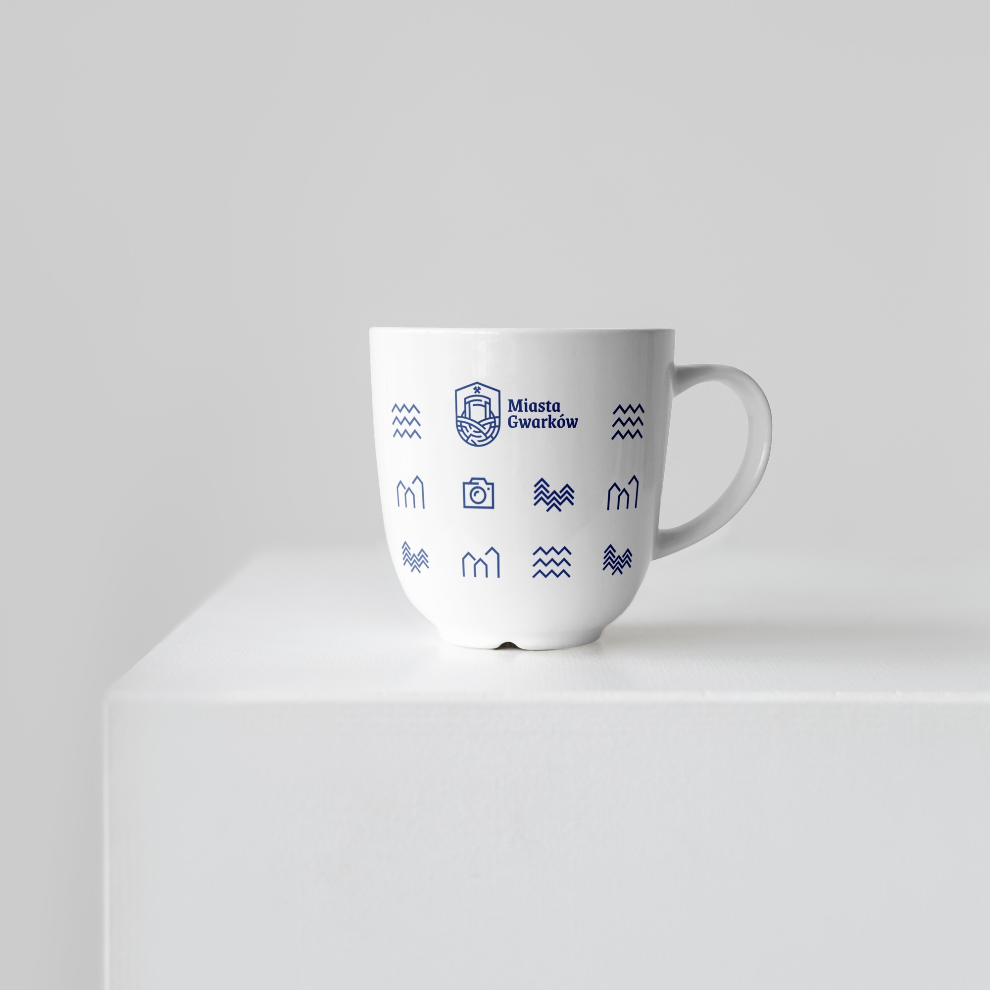 A white porcelain mug with navy pictograms and the Miasta Gwarków logo