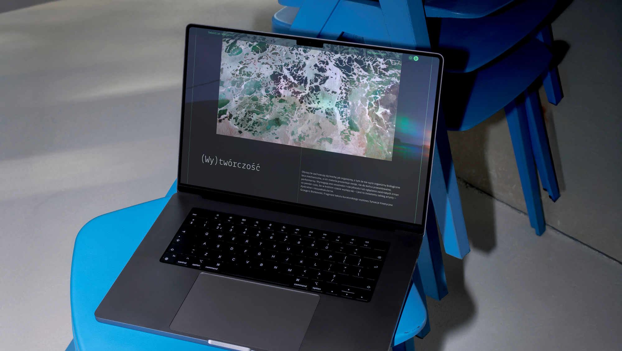 A laptop on blue chairs showing the (Wy)twórczość page of Sebastian Wywiórski's website in dark mode