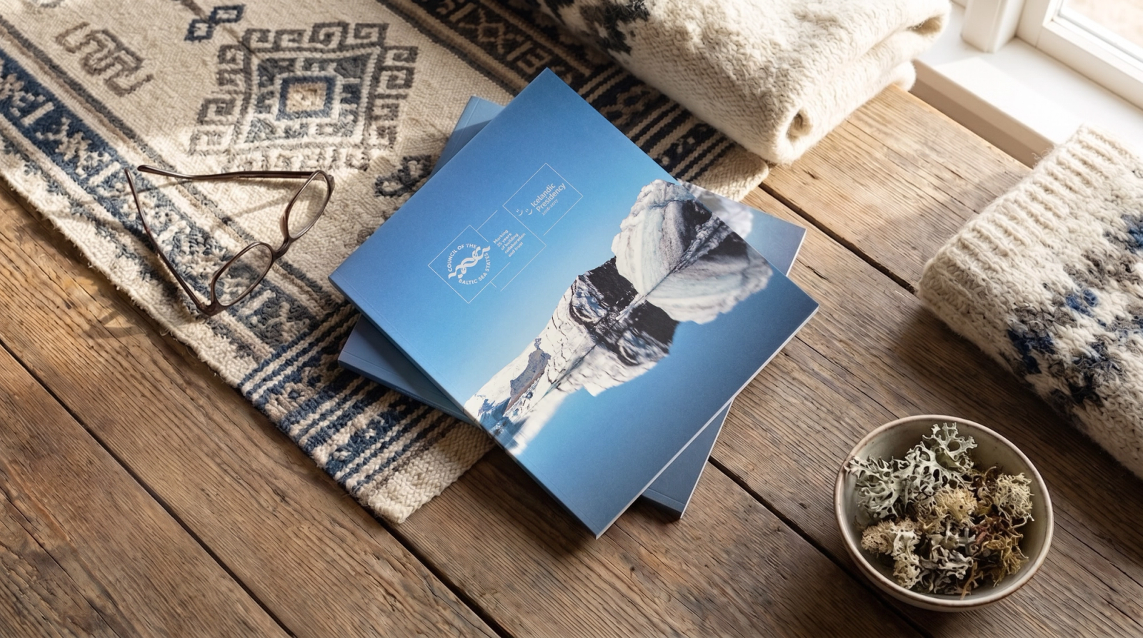 Annual report lying on a table next to an Icelandic blanket, lichens and glasses