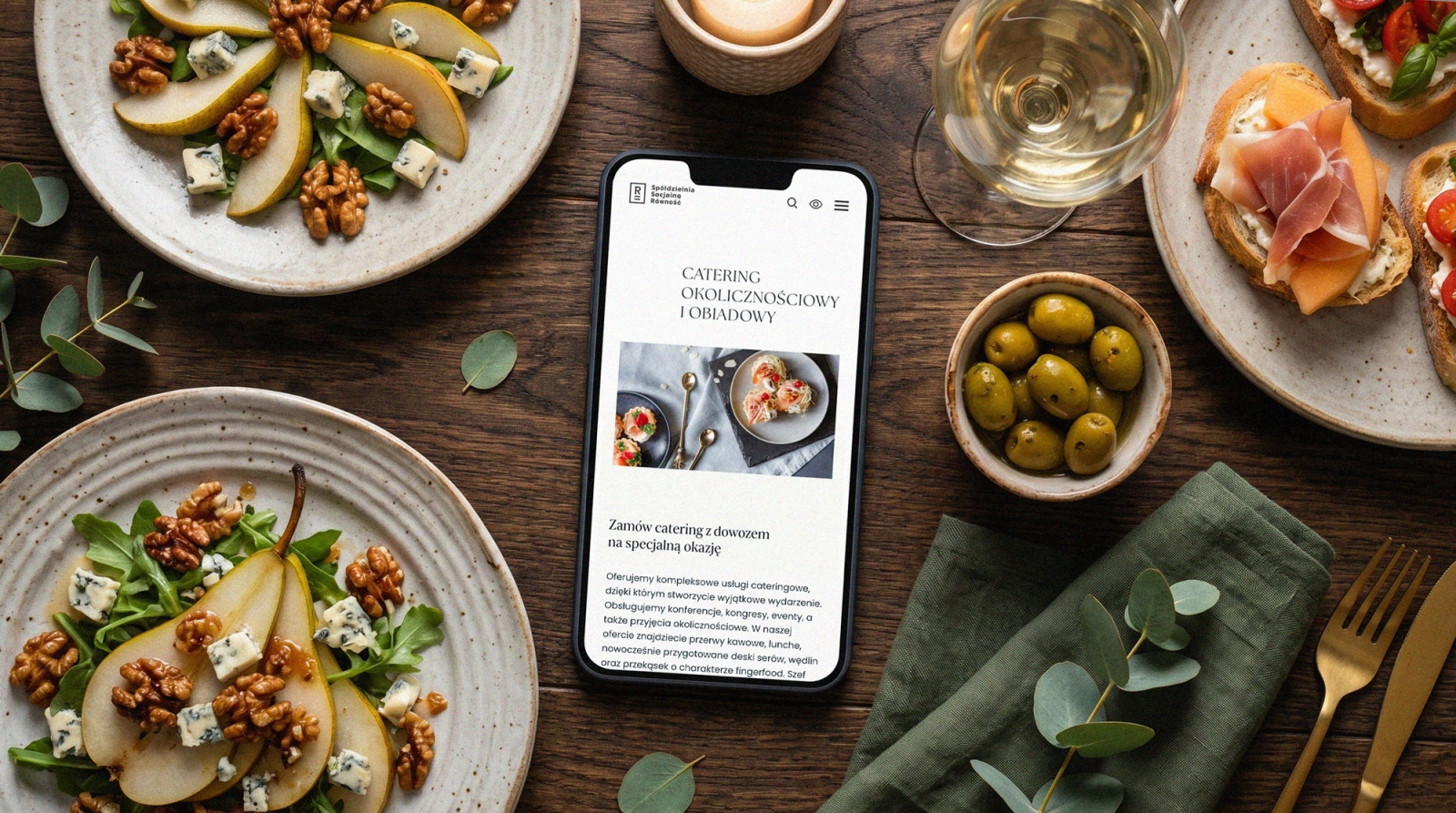 A rustic table with plates of pear, walnut and gorgonzola salad; in the middle a phone showing the Catering Równość website