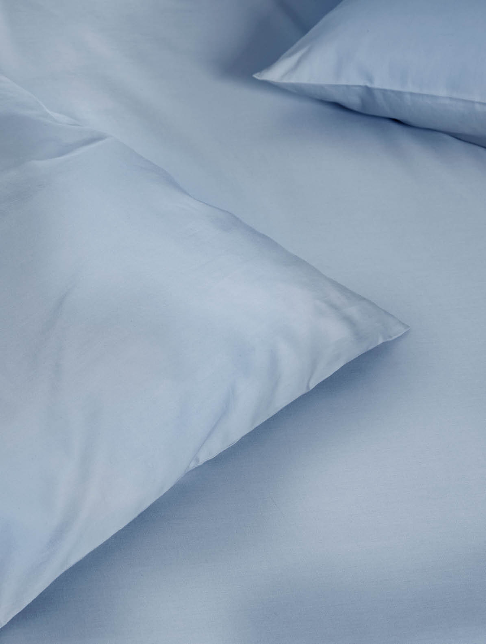 Nærbilde av steinvasket satenglaken og putetrekk i dus blå. Den myke, matte overflaten og den rolige blåfargen fremhever teksturen i stoffet.