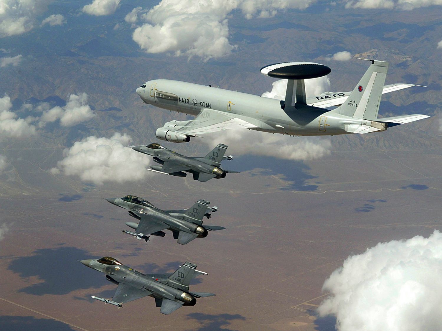 A NATO E-3 AWACS surveillance aircraft flying alongside three US Air Force F-16 fighters.