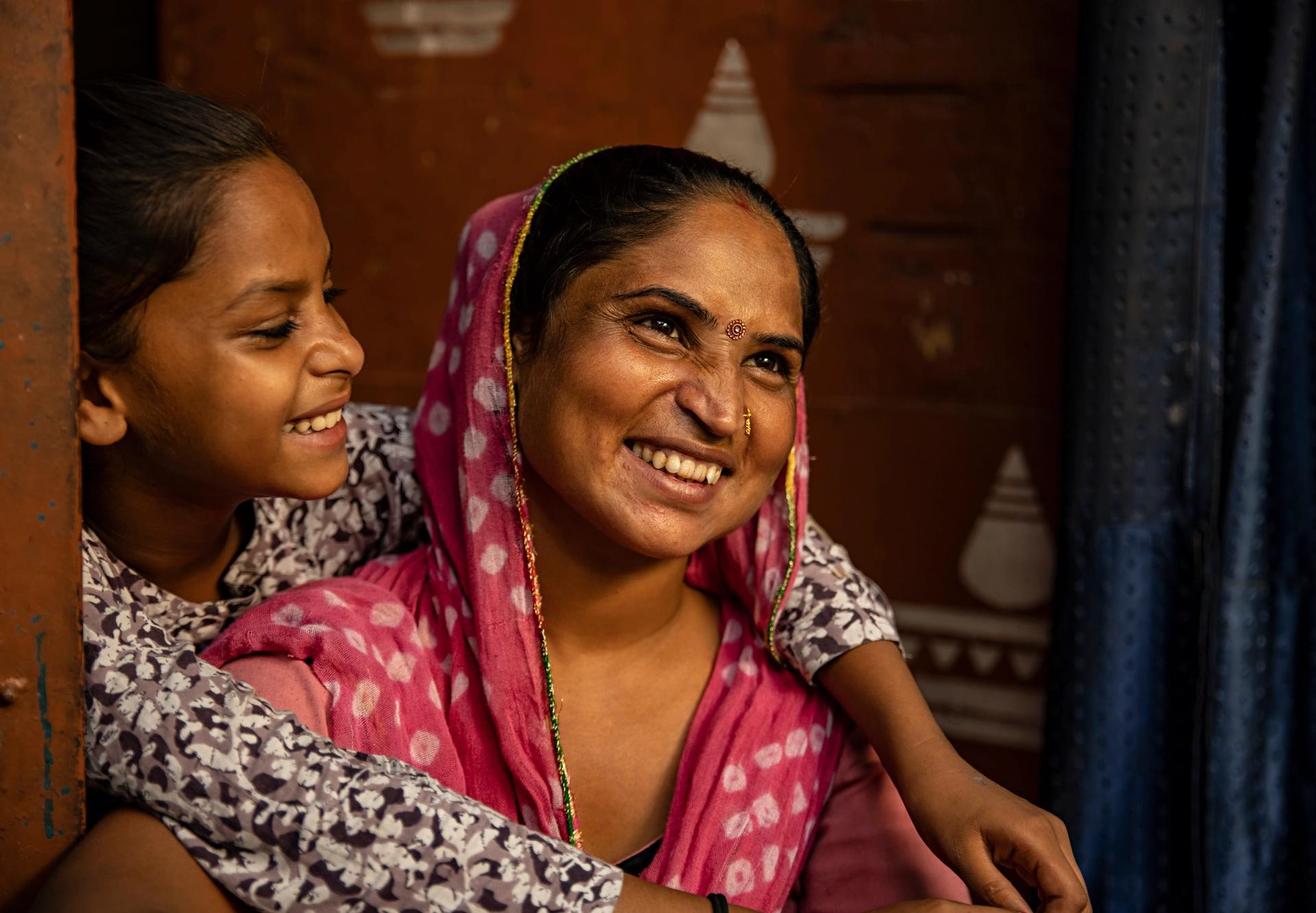 Mother being hugged by her younger daughter from behind.