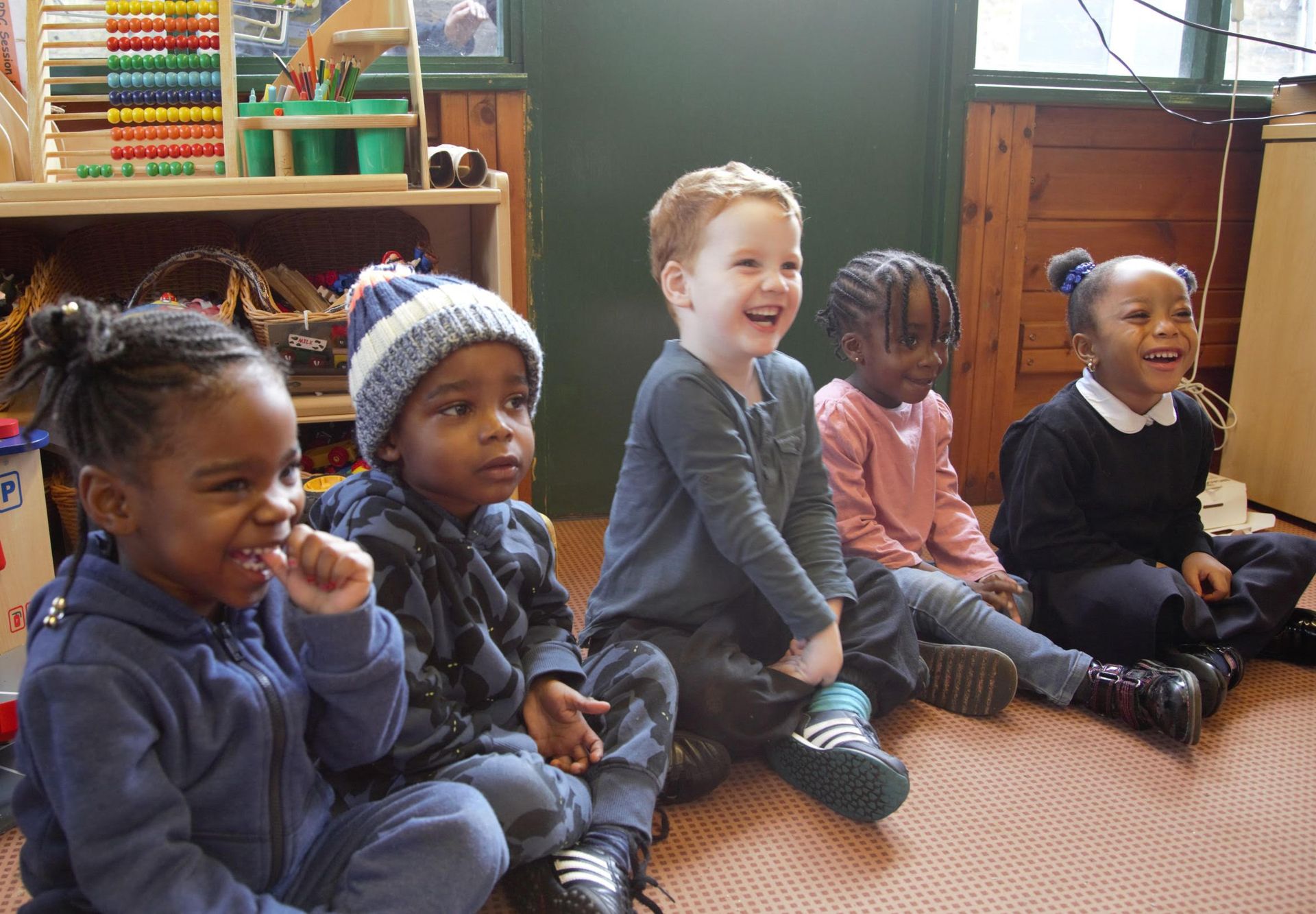 Young children in a nursery class sitting cross-legged on the floor and smiling.