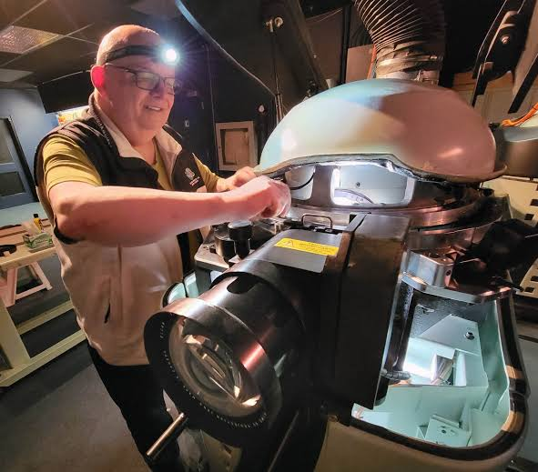 Cinema projectionist operating a large-format IMAX 70mm film projector inside the booth