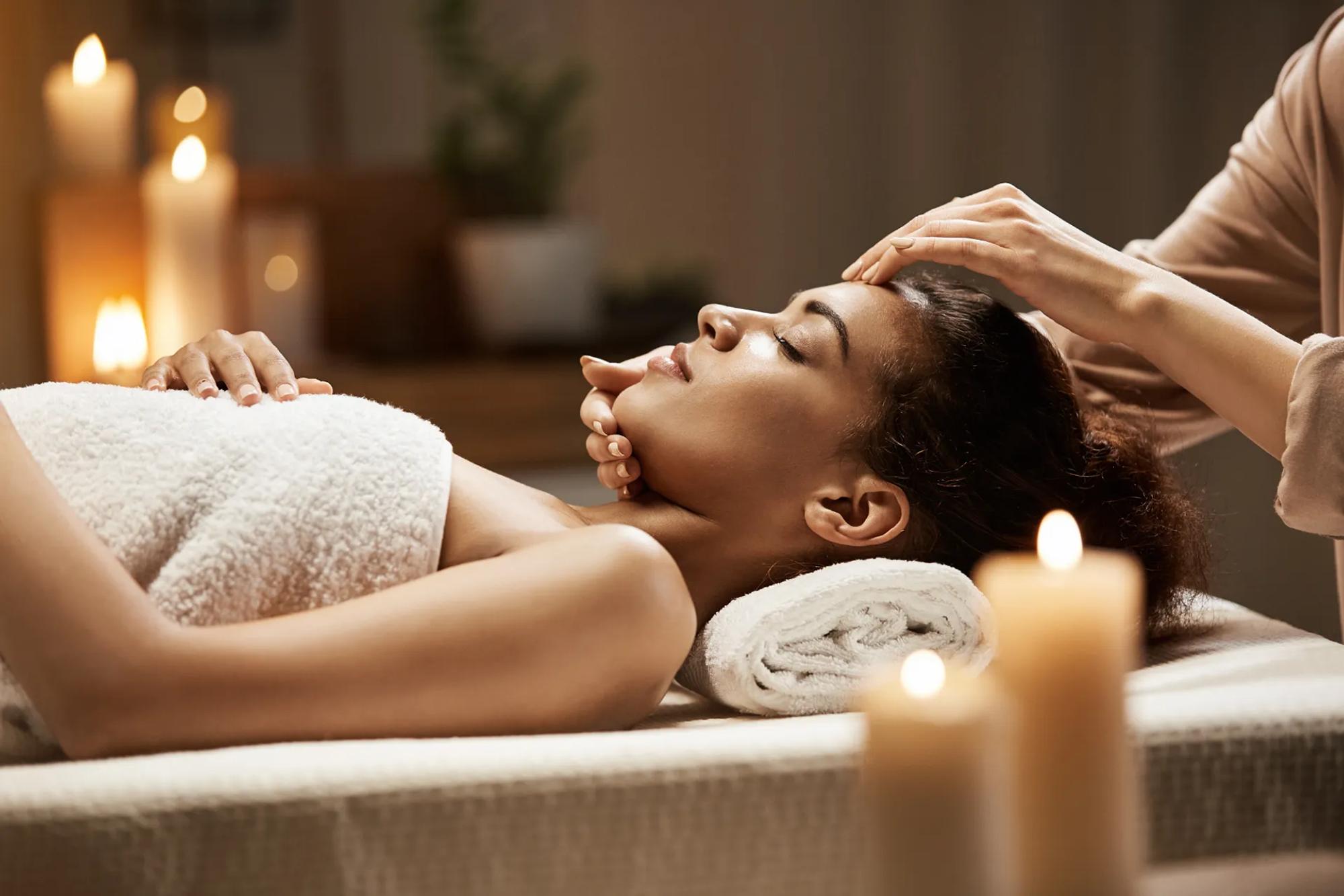 Terapistin misafire huzur veren bir baş masajı uyguladığı mum ışıklı spa odası