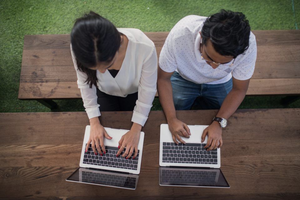 Two people working side by side on laptops, seen from above