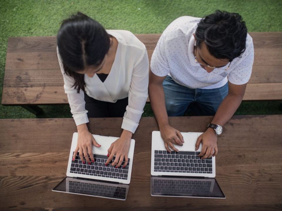 Two people working side by side on laptops, seen from above