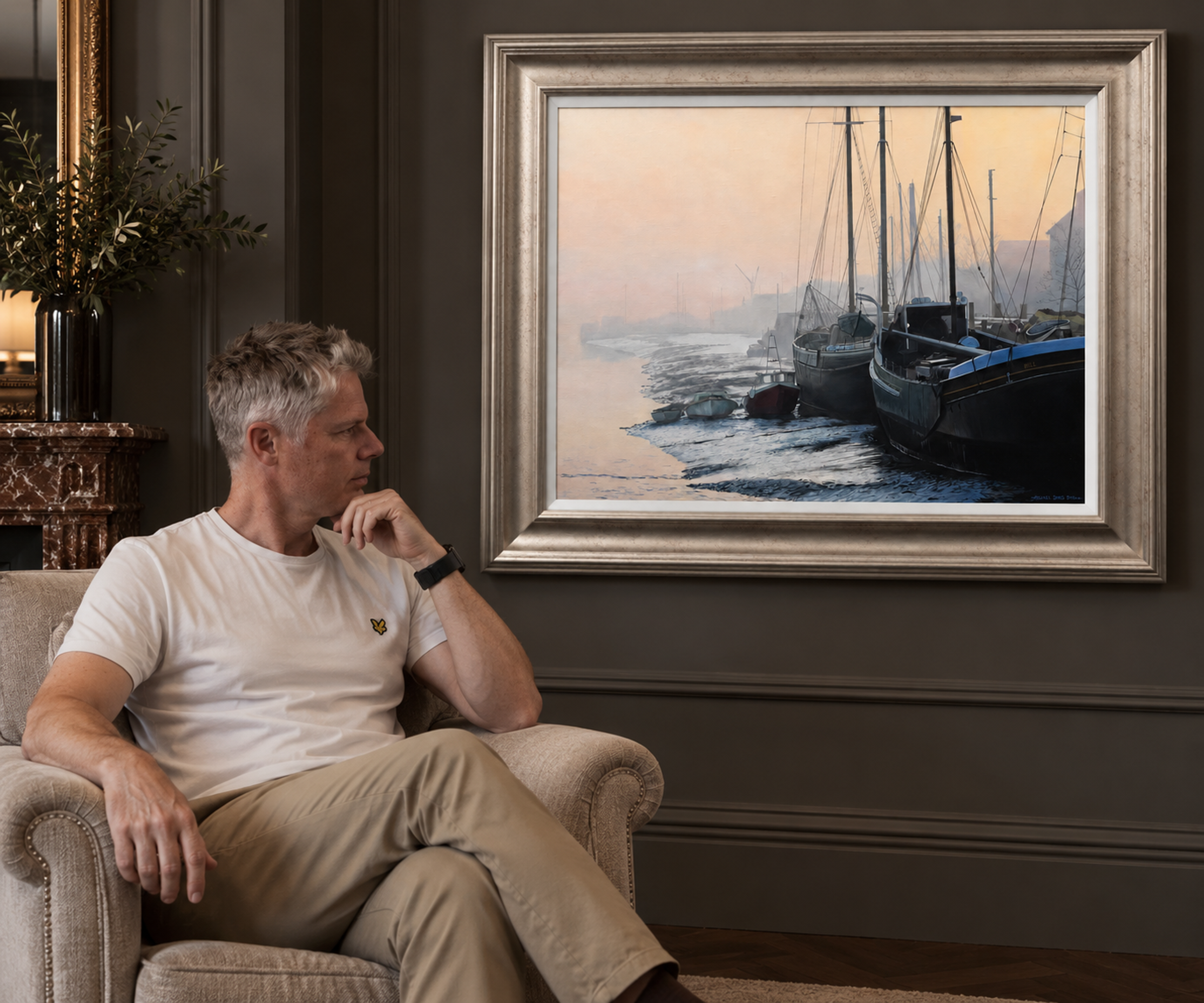 Michael James Smith seated beside one of his framed original paintings in a gallery