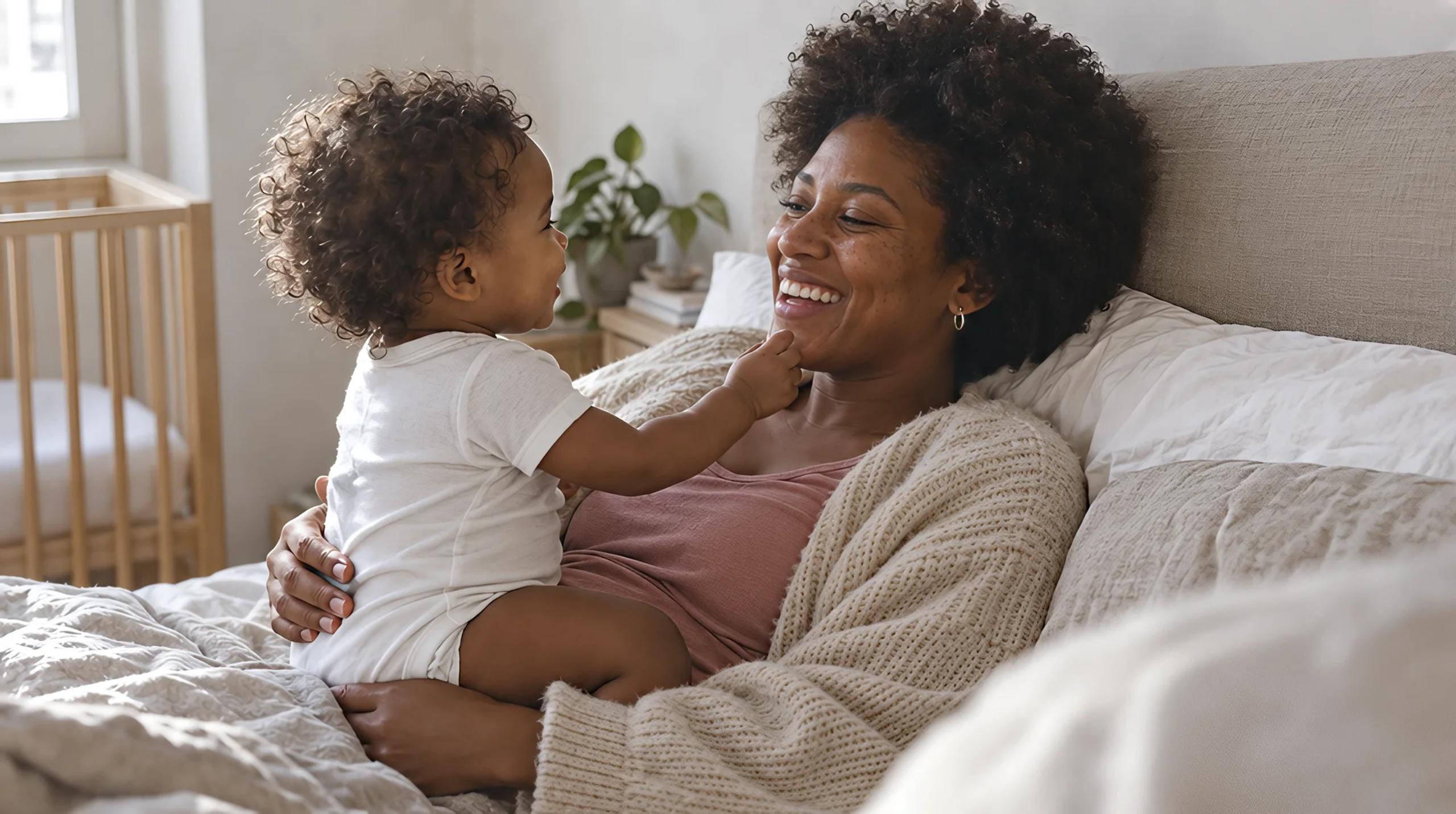 Madre sonriendo en la cama mientras su bebé le toca la cara