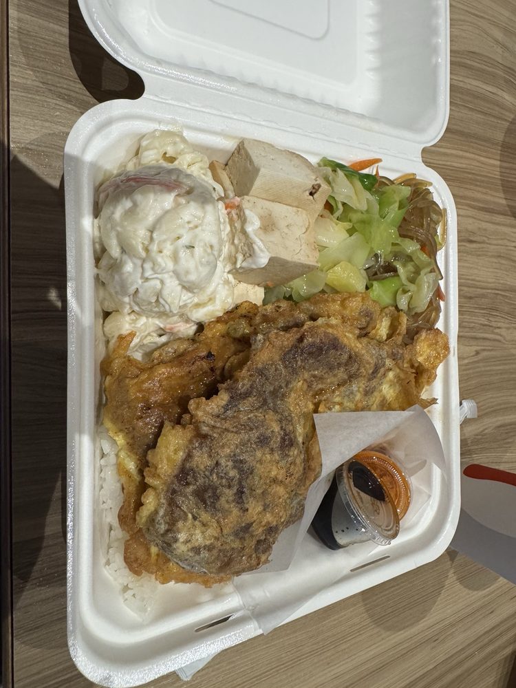 Egg-battered meat jun over rice with macaroni salad, tofu and cabbage in a takeout box