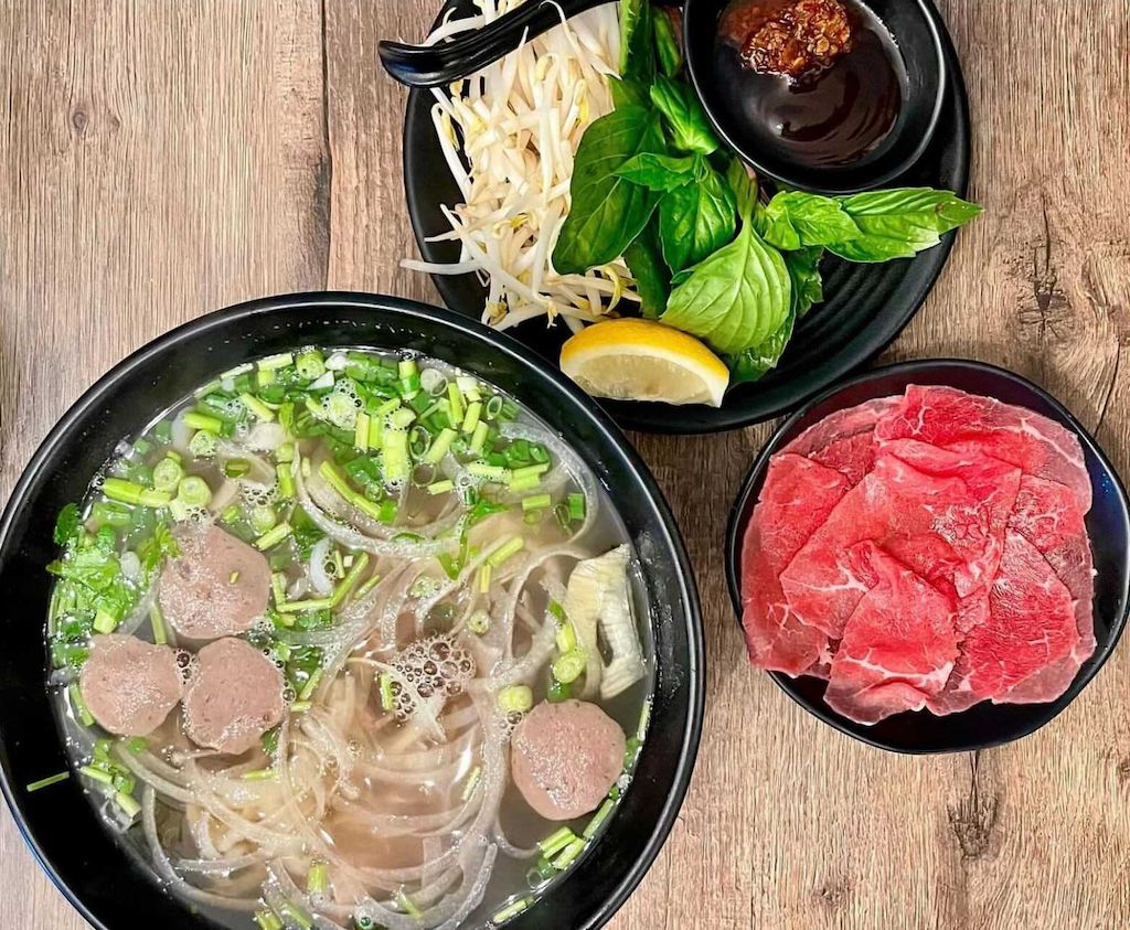 Pho with beef meatballs and green onion, with a plate of rare sliced beef, bean sprouts, basil and lemon