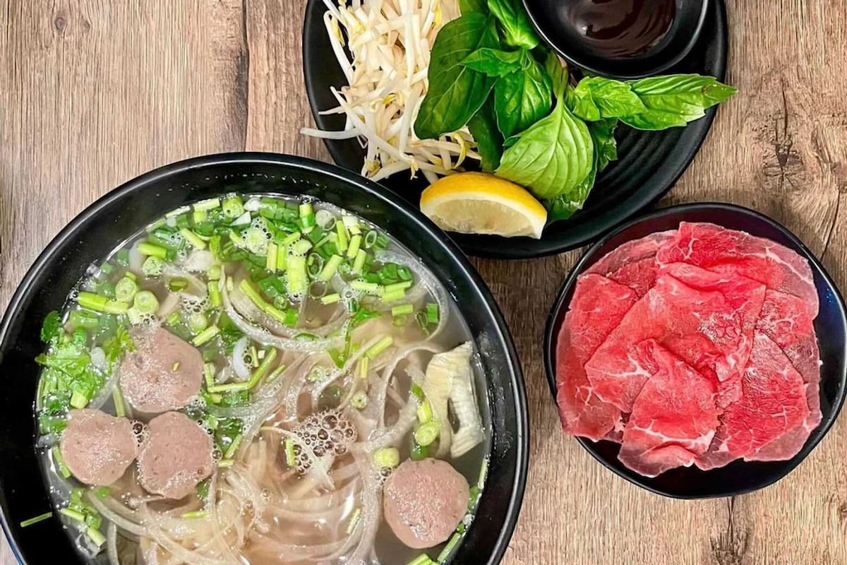 Pho with beef meatballs and green onion, with a plate of rare sliced beef, bean sprouts, basil and lemon