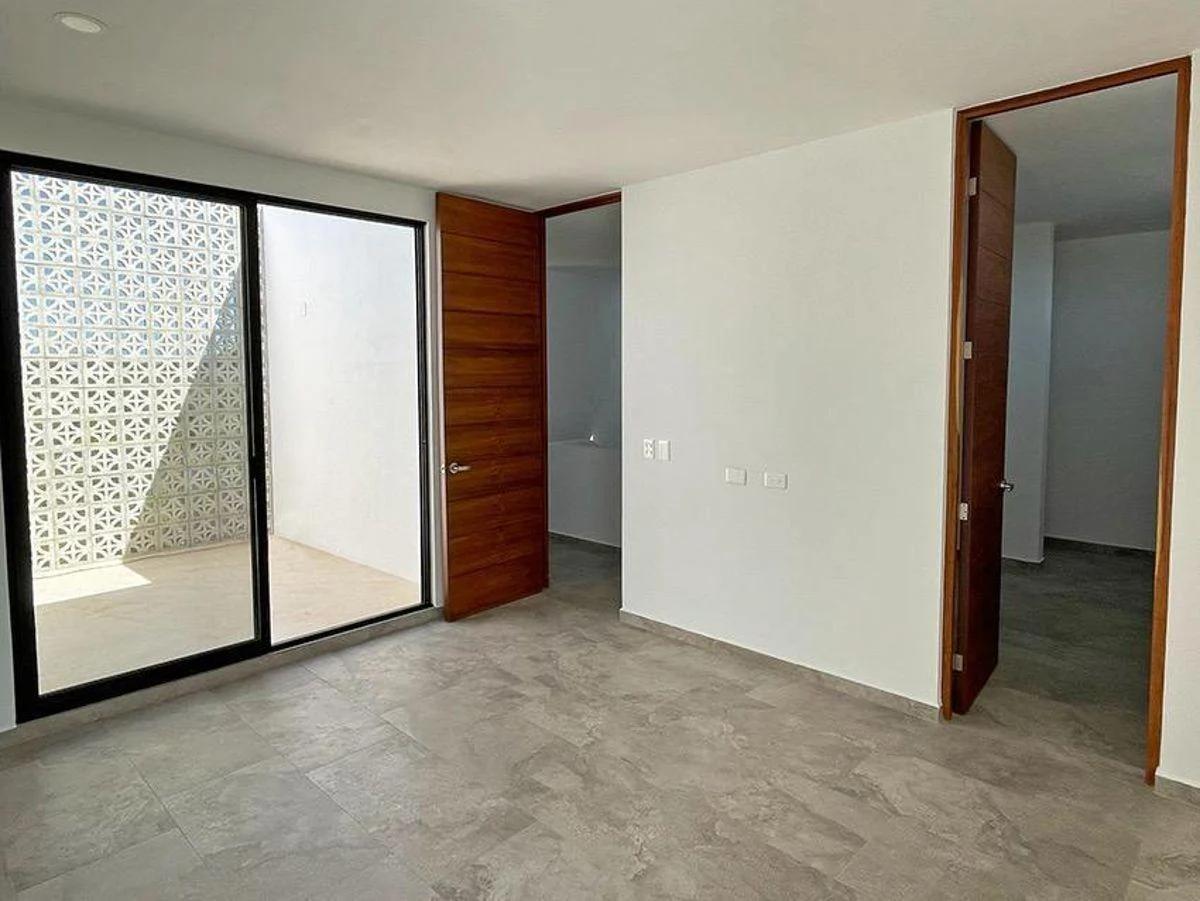 Interior de una casa. La habitación presenta un diseño moderno con paredes blancas limpias, baldosas grises de gran formato y una puerta corrediza de vidrio que se abre a un pequeño espacio privado al aire libre con una pared de mampara decorativa. 