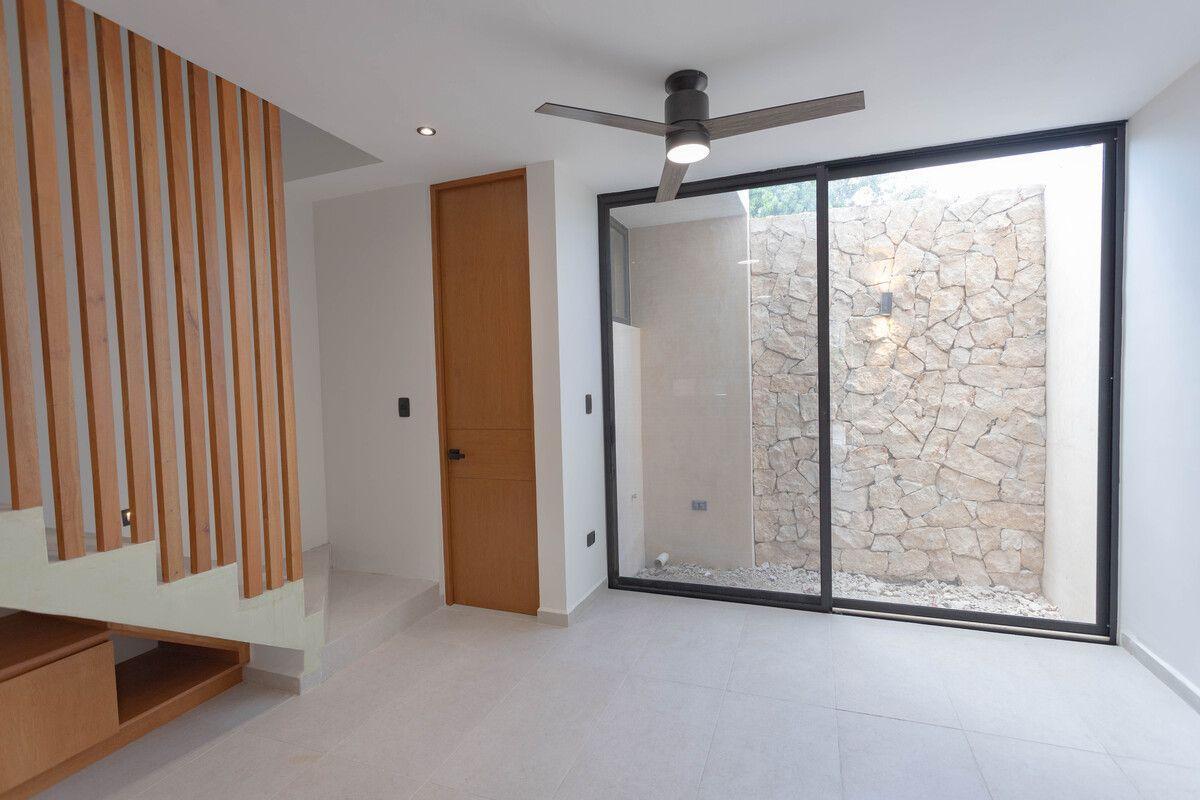 Esta propiedad específica presenta un diseño minimalista con paredes blancas, pisos de baldosas de colores claros y detalles de madera natural en las escaleras y la puerta. 