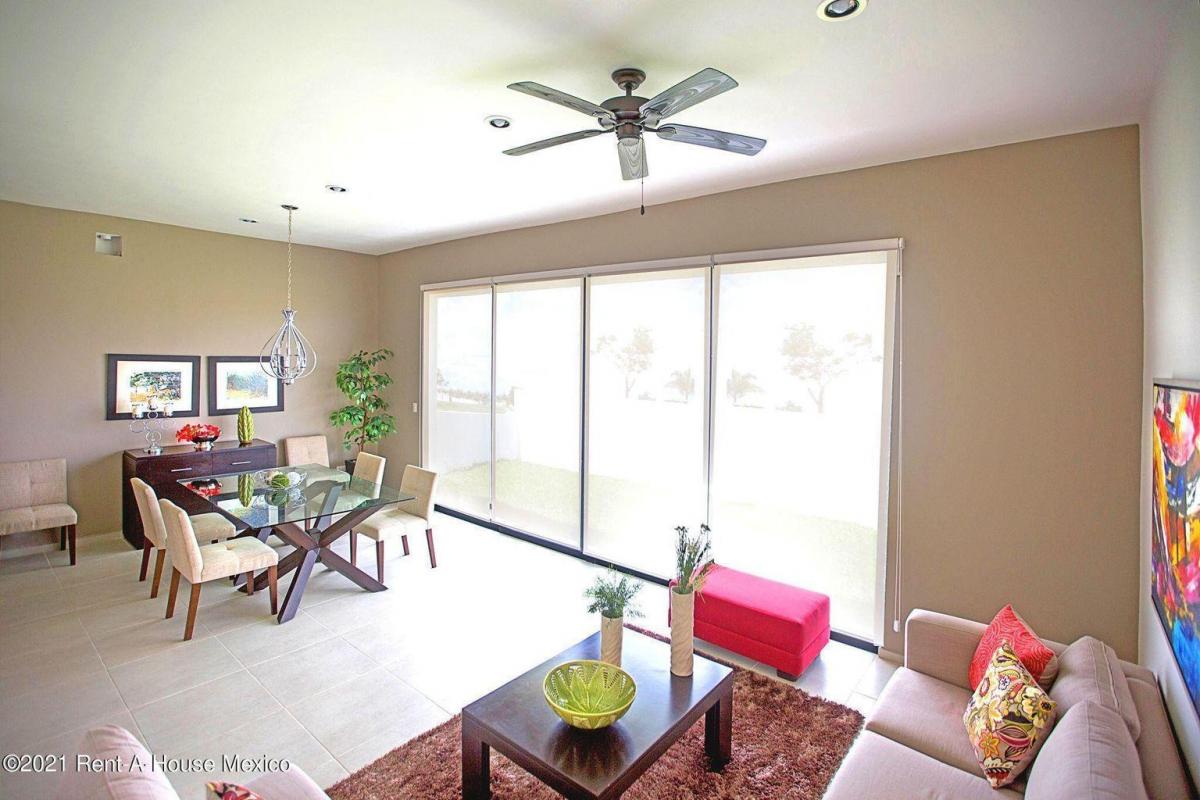 La foto muestra una sala de estar y comedor de planta abierta con muebles modernos. El espacio cuenta con grandes puertas corredizas de vidrio, un ventilador de techo y pisos de baldosas.