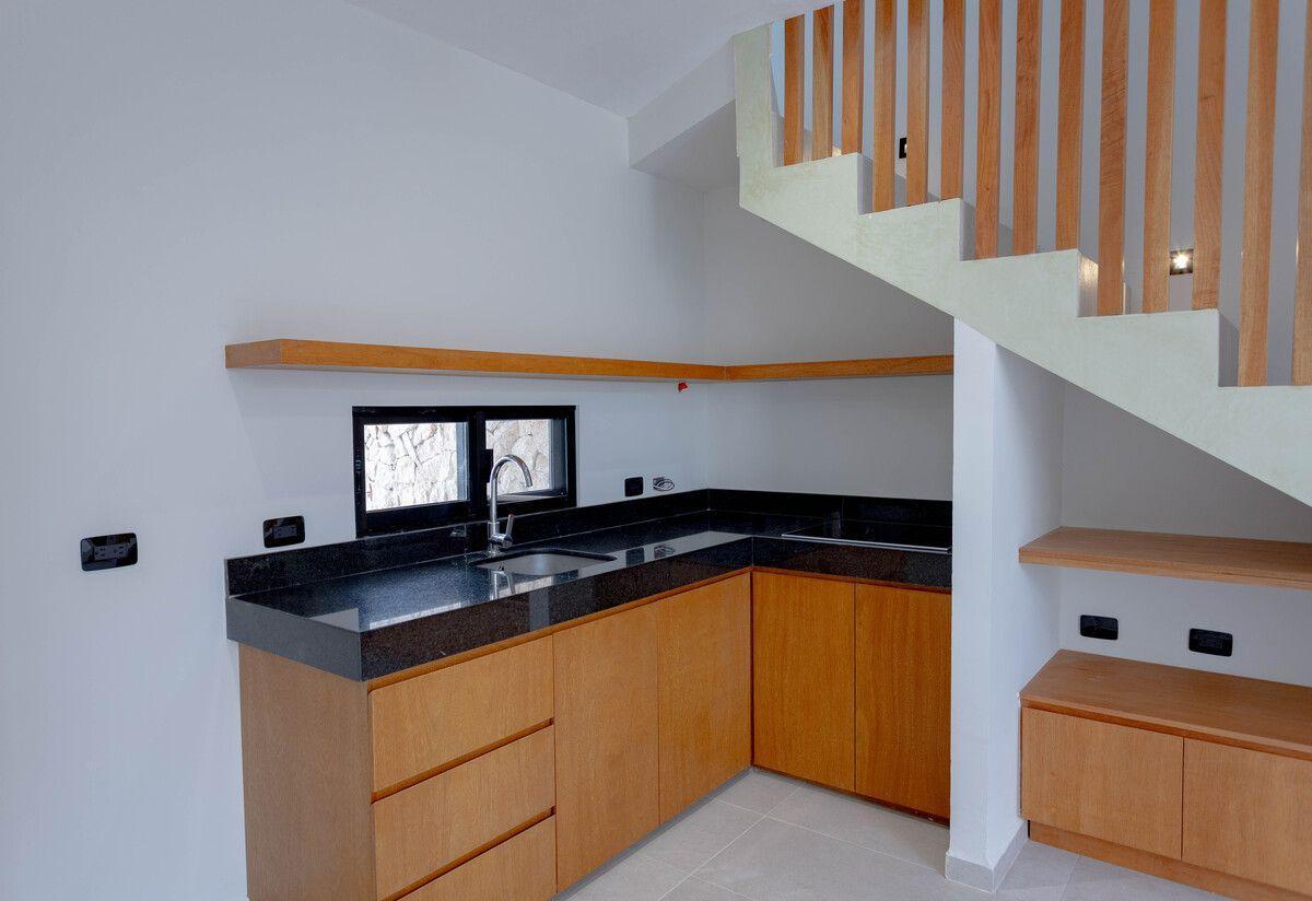 El diseño presenta gabinetes y estanterías de madera clara, que contrastan con encimeras de granito oscuro.