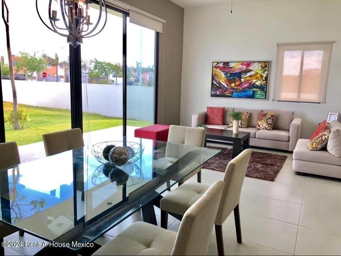 Comedor y sala de estar modernos de una casa. El comedor cuenta con una gran mesa con tapa de cristal con varias sillas tapizadas y una lámpara de araña contemporánea. El estilo general es abierto y minimalista, con pisos de baldosas en las áreas de estar principales.