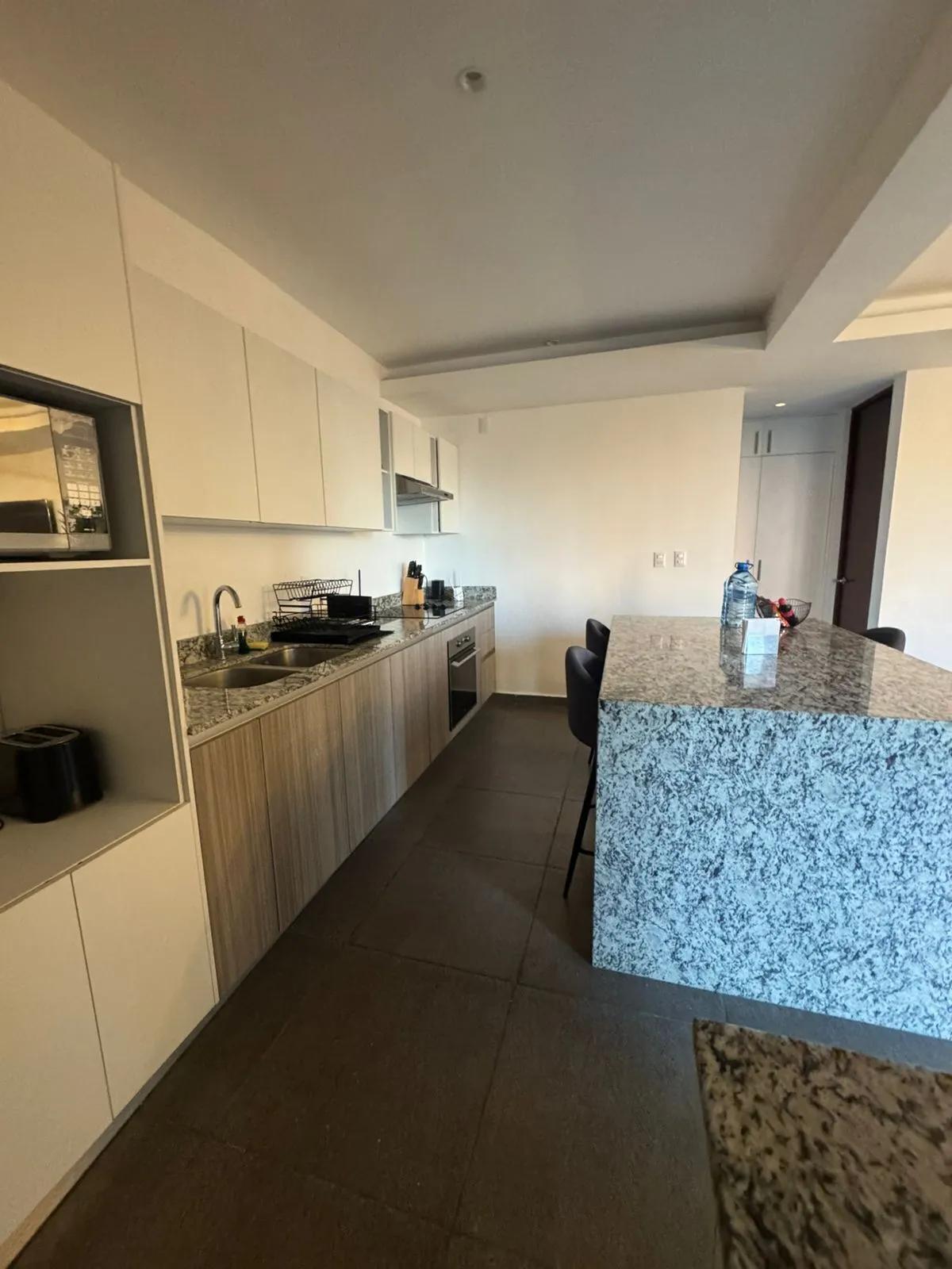 Cocina moderna, cuenta con gabinetes superiores blancos, gabinetes inferiores de madera y una isla grande con una encimera de granito moteado. 