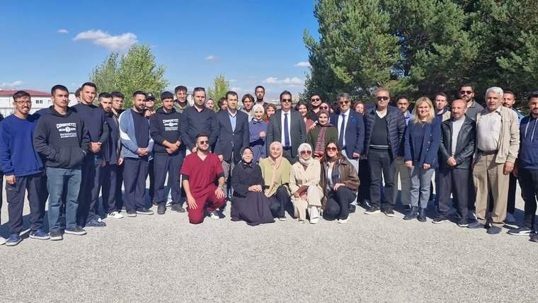 Açık havada, ağaçların önünde ayakta duran ve ön sırada oturan kalabalık bir grup birlikte poz veriyor.