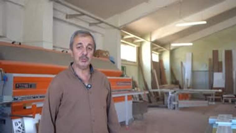 Bir kişi, bir üretim atölyesinde duruyor ve arka planda makineler yer alıyor.
