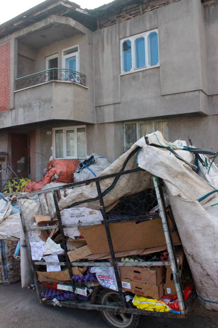 Bir binanın önünde, atık toplama malzemeleri ve torbalar yığılmış.