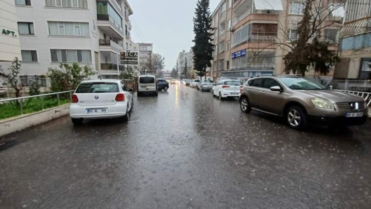 Yağmur altında, iki yanında apartmanlar ve park etmiş otomobiller bulunan ıslak bir şehir sokağı.