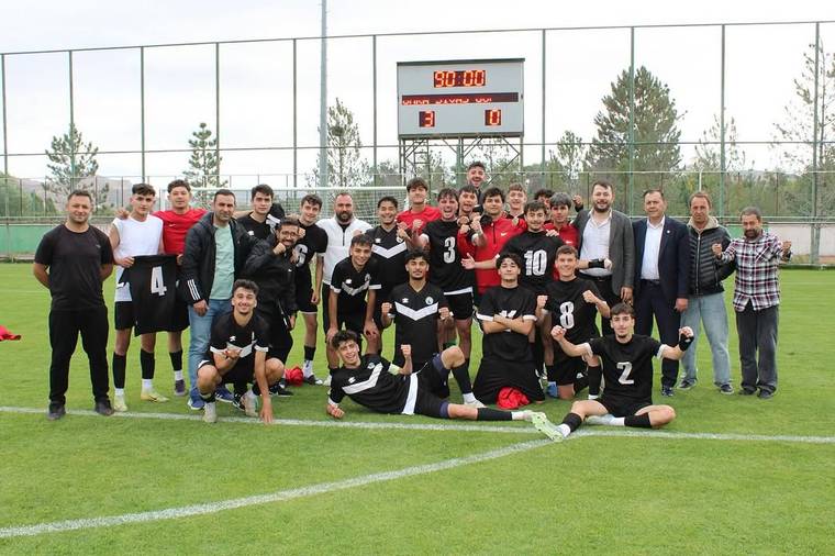 Futbol sahasında siyah formalı genç futbolcular ve yetişkinler, 3-0 yazan skor tabelasının önünde poz veriyor.